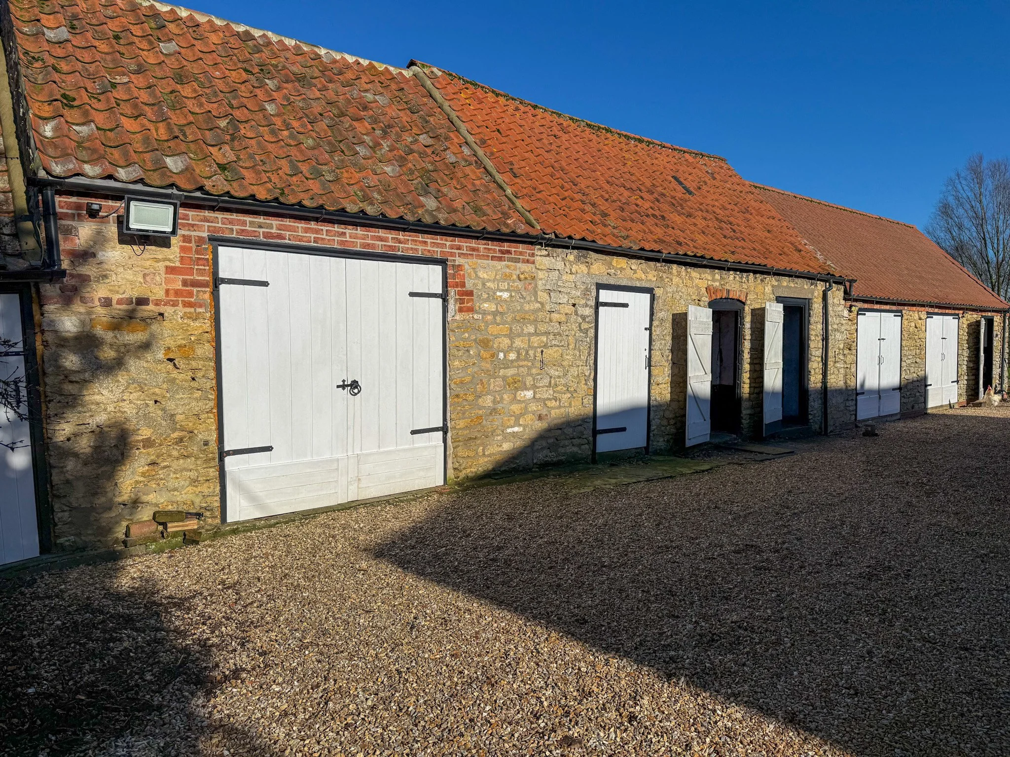 A row of white barn-style doors on a stone and brick building with a red tiled roof under a blue sky.
