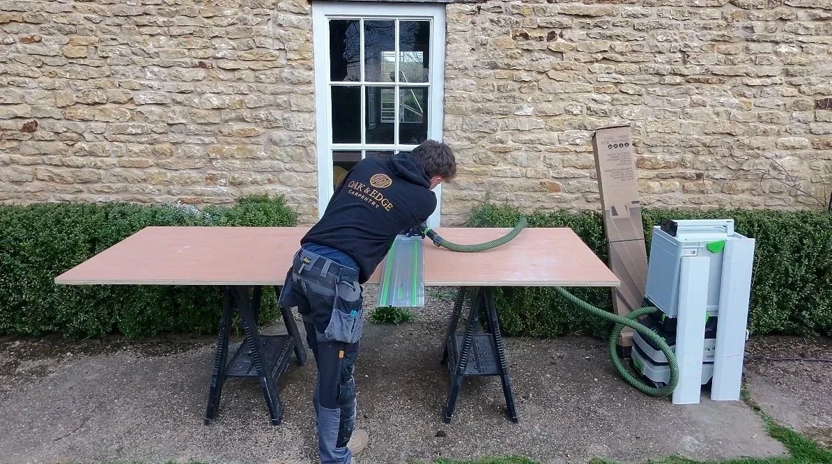 A man working with a portable dust extraction system connected to a piece of equipment on a work table outdoors.