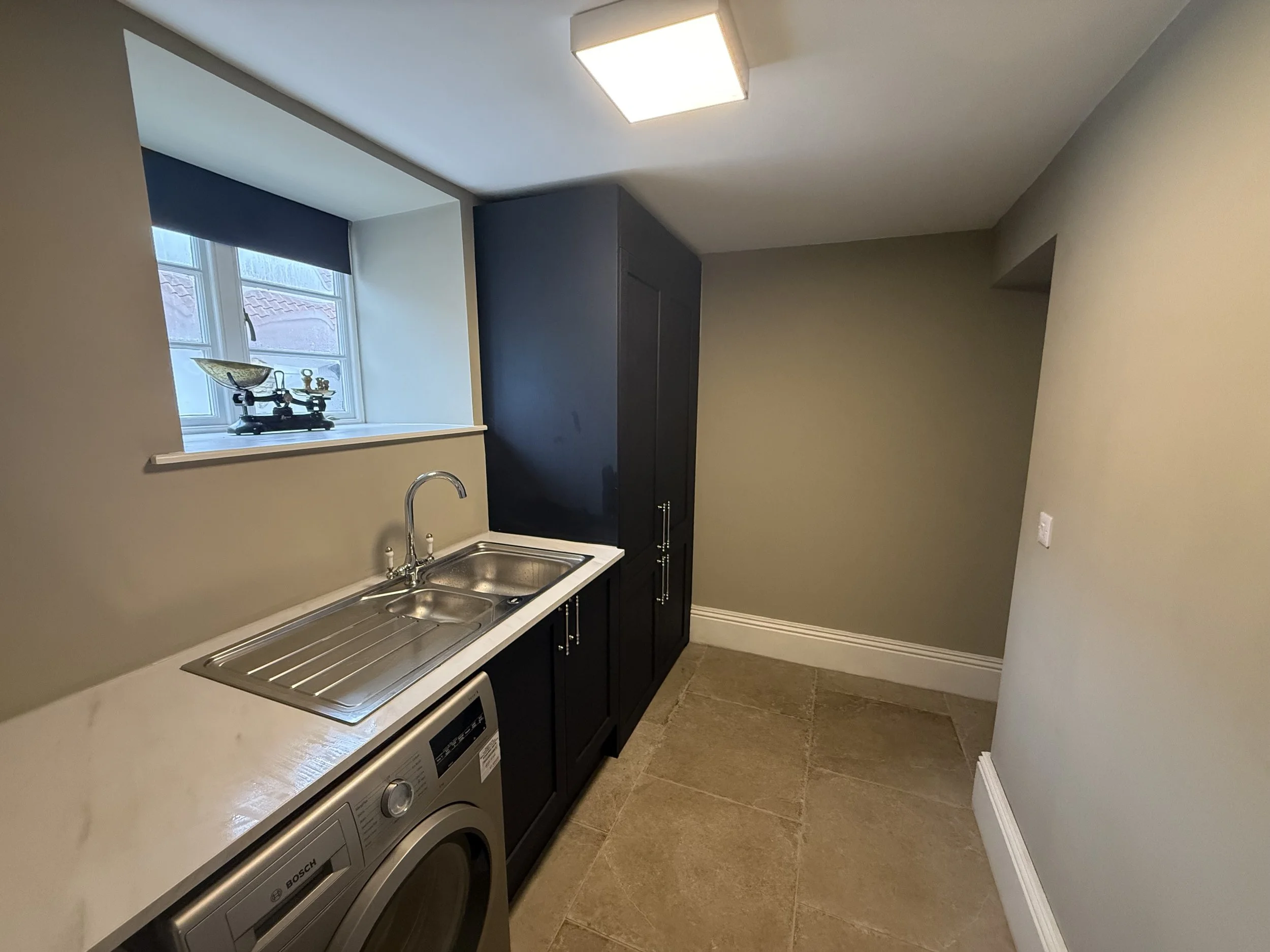 Laundry room with a stainless steel sink, black cabinets, a window with a scale on the windowsill, and a washing machine.