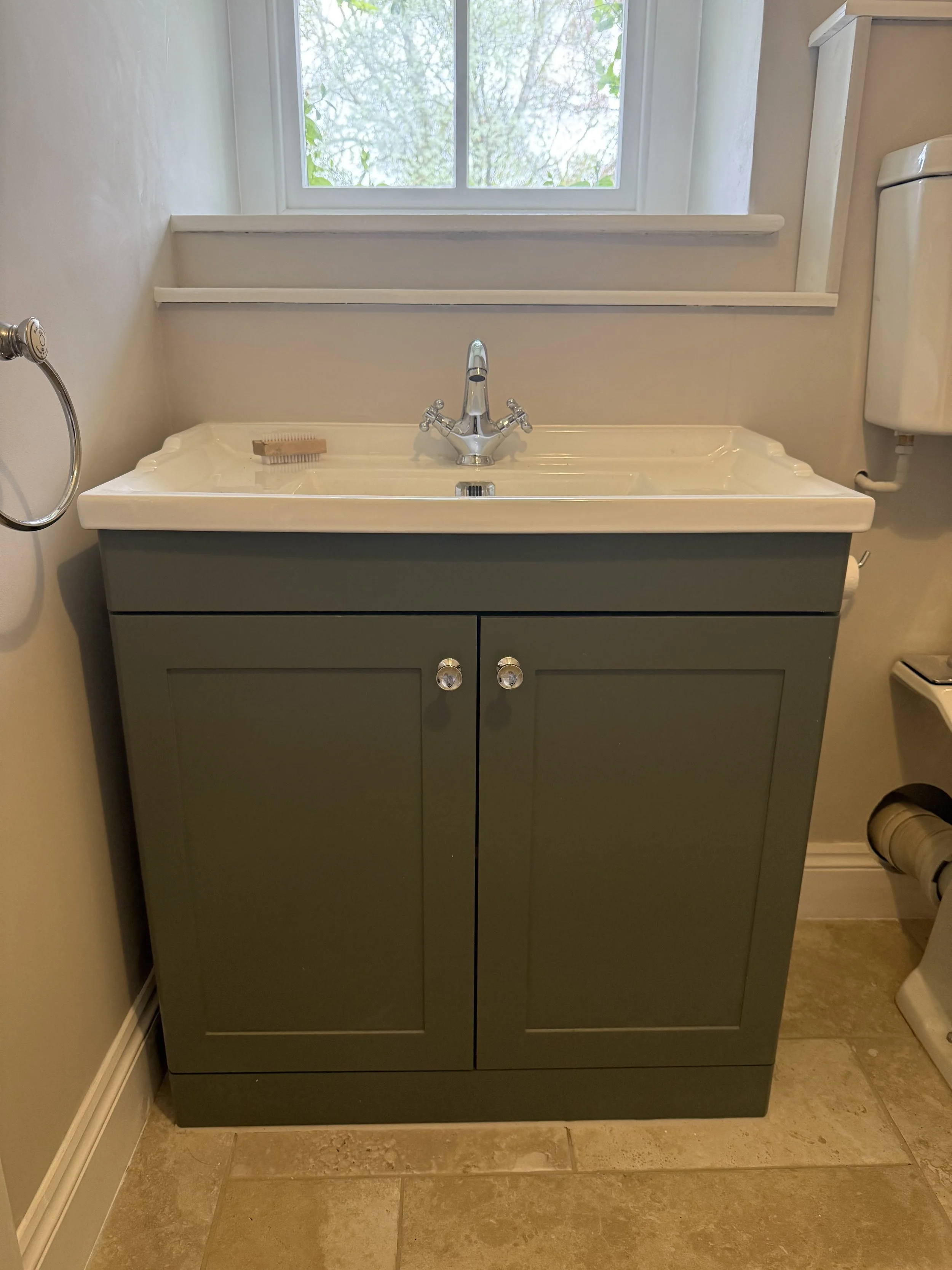 Bathroom vanity with a white ceramic sink, a chrome faucet, a soap dish, and a window above, with a beige tiled floor.