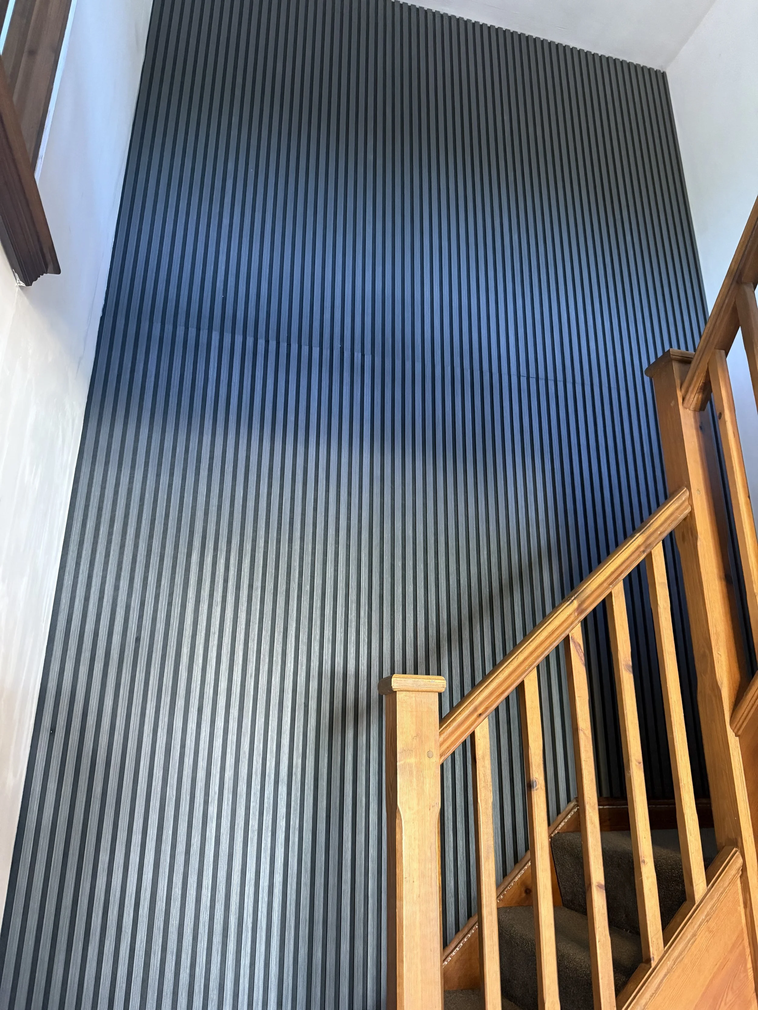 Interior view of a staircase with wooden railings and black and gray vertically striped wallpaper on the wall beside the stairs.