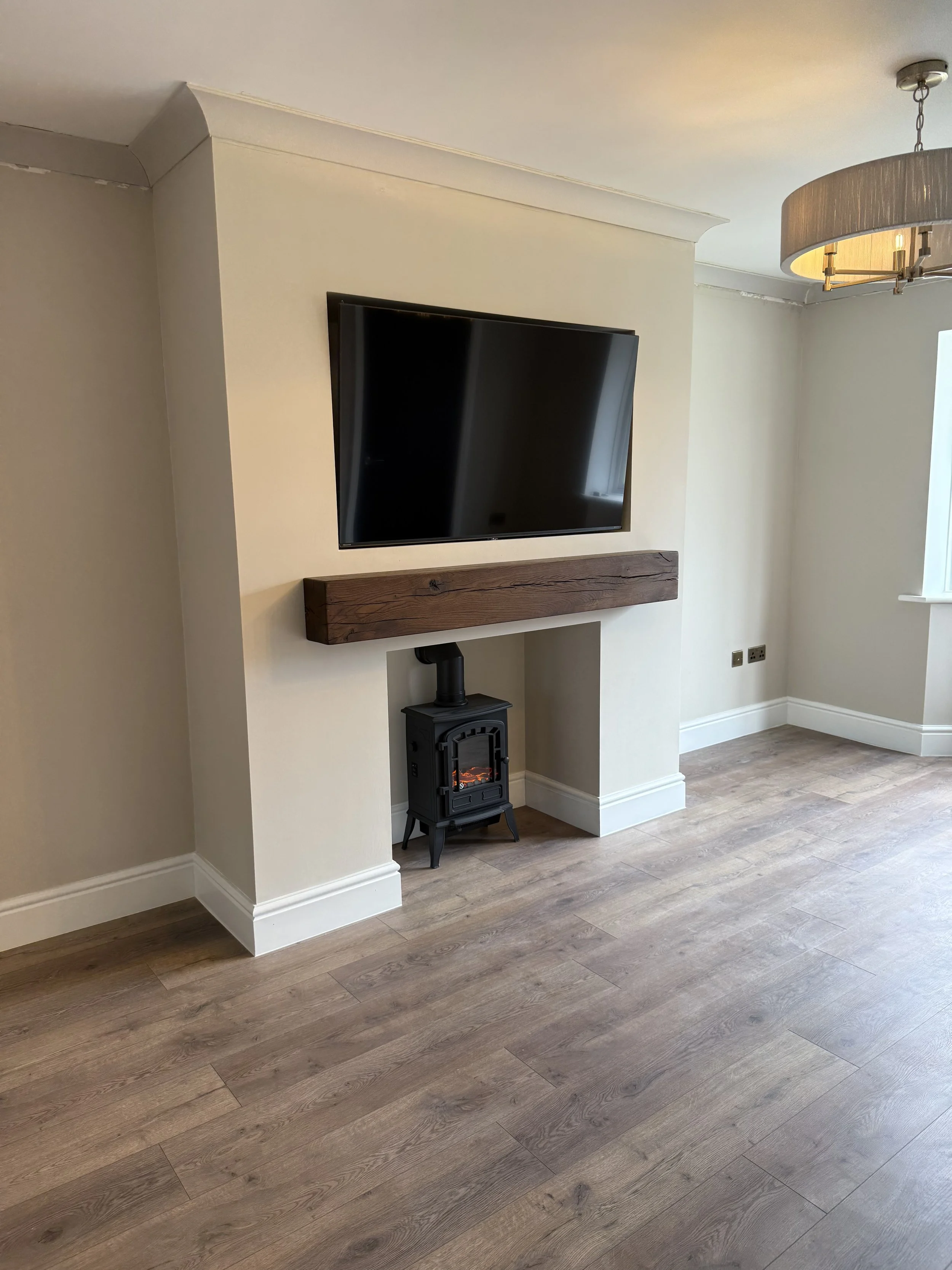 Living room with a mounted flat-screen TV, a small black stove, and wooden floors.