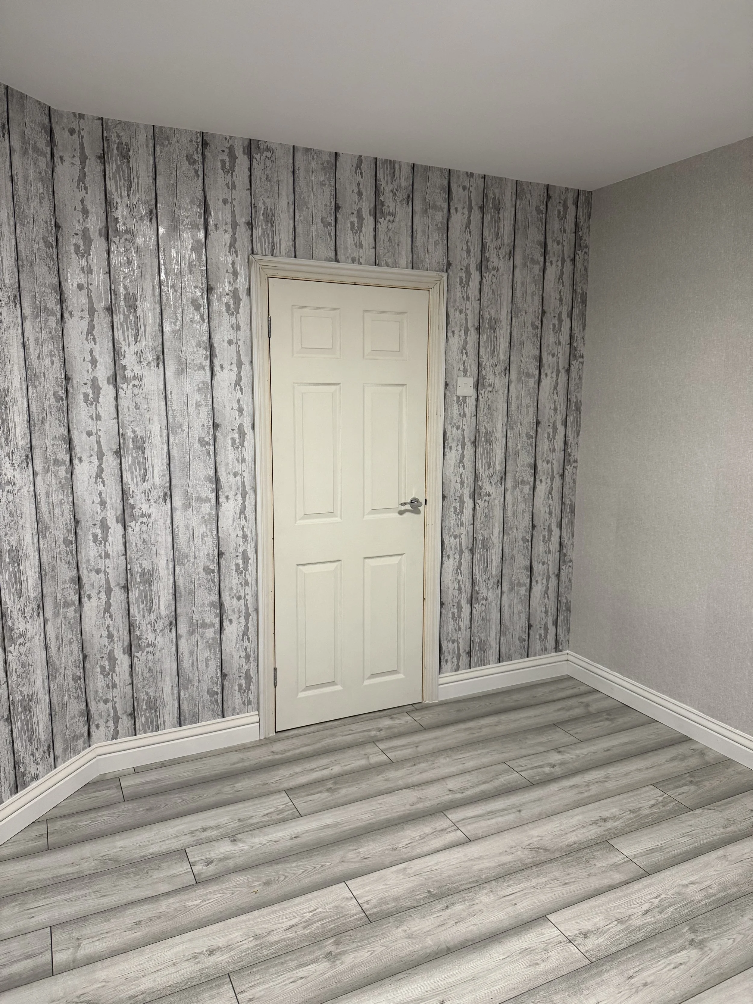 Interior room with a door, grey wood panel feature wall, white ceiling, grey wood-look flooring, and trim.