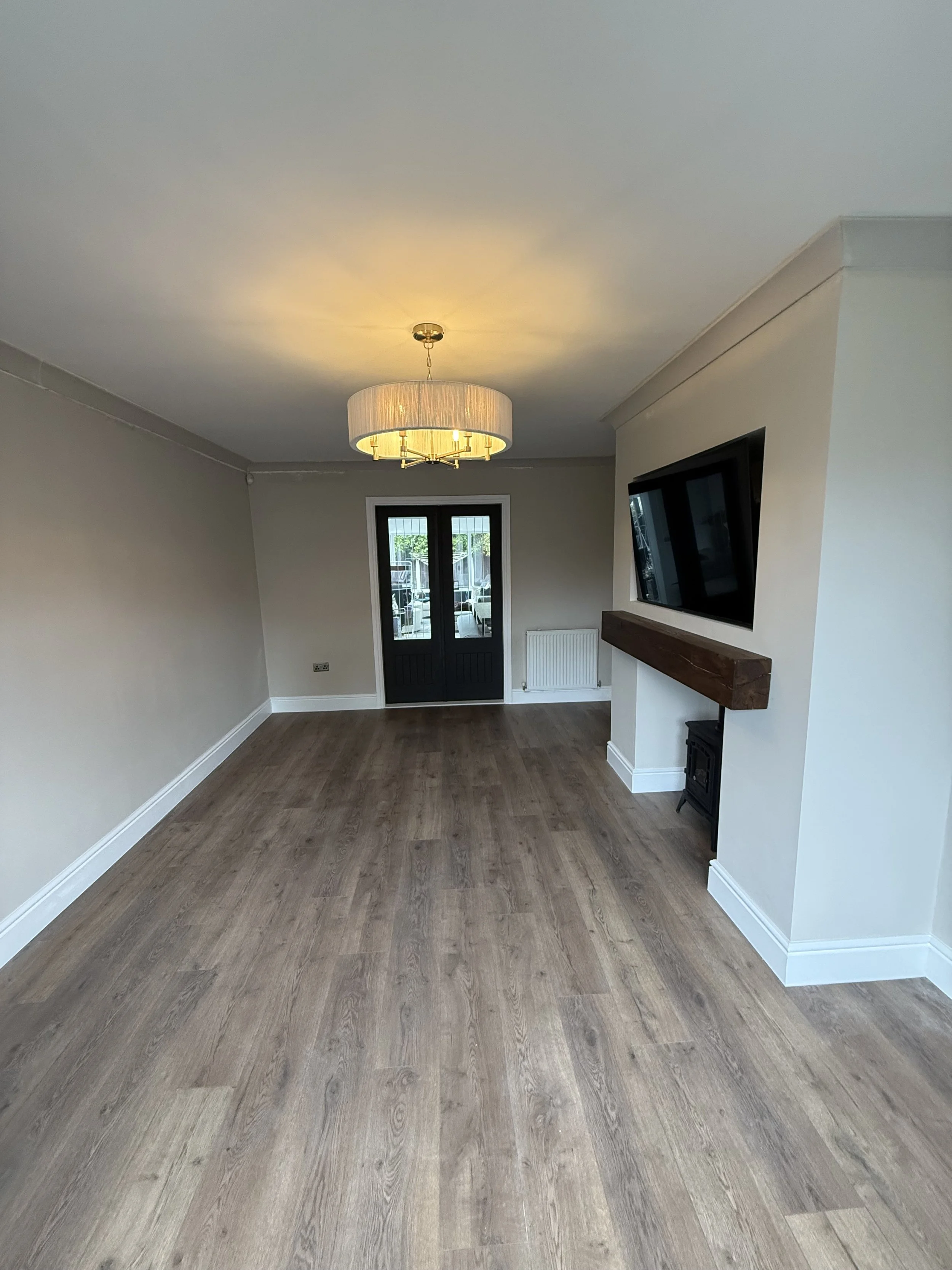 Empty living room with wood flooring, a ceiling light fixture, a TV on the wall, and a door with glass panels leading outside.