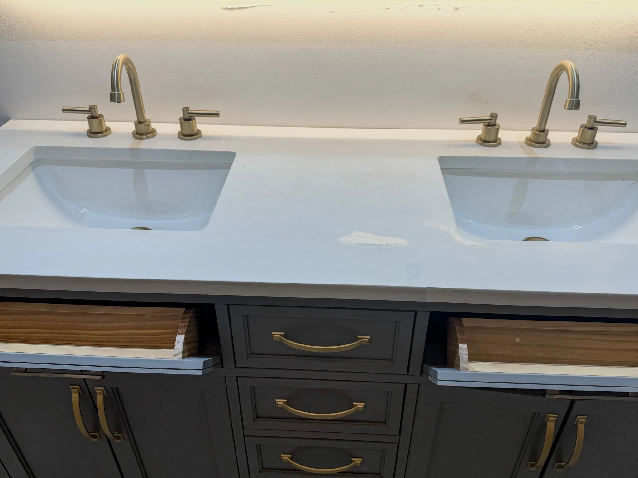 Double bathroom vanity with two white sinks, each with brushed gold faucets and handles, and gray cabinetry with gold handles.