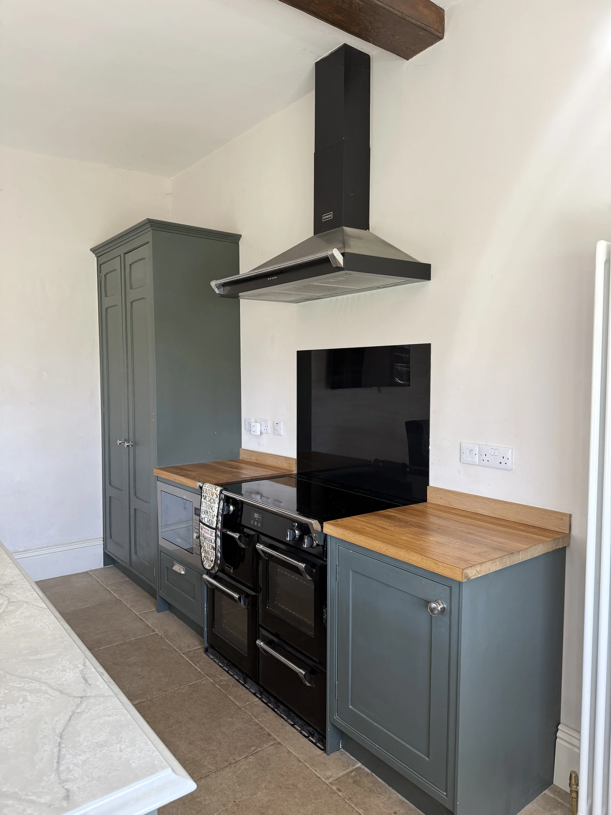Kitchen with green cabinets, a black stove and oven, a wooden countertop, a vent hood, and electrical outlets.