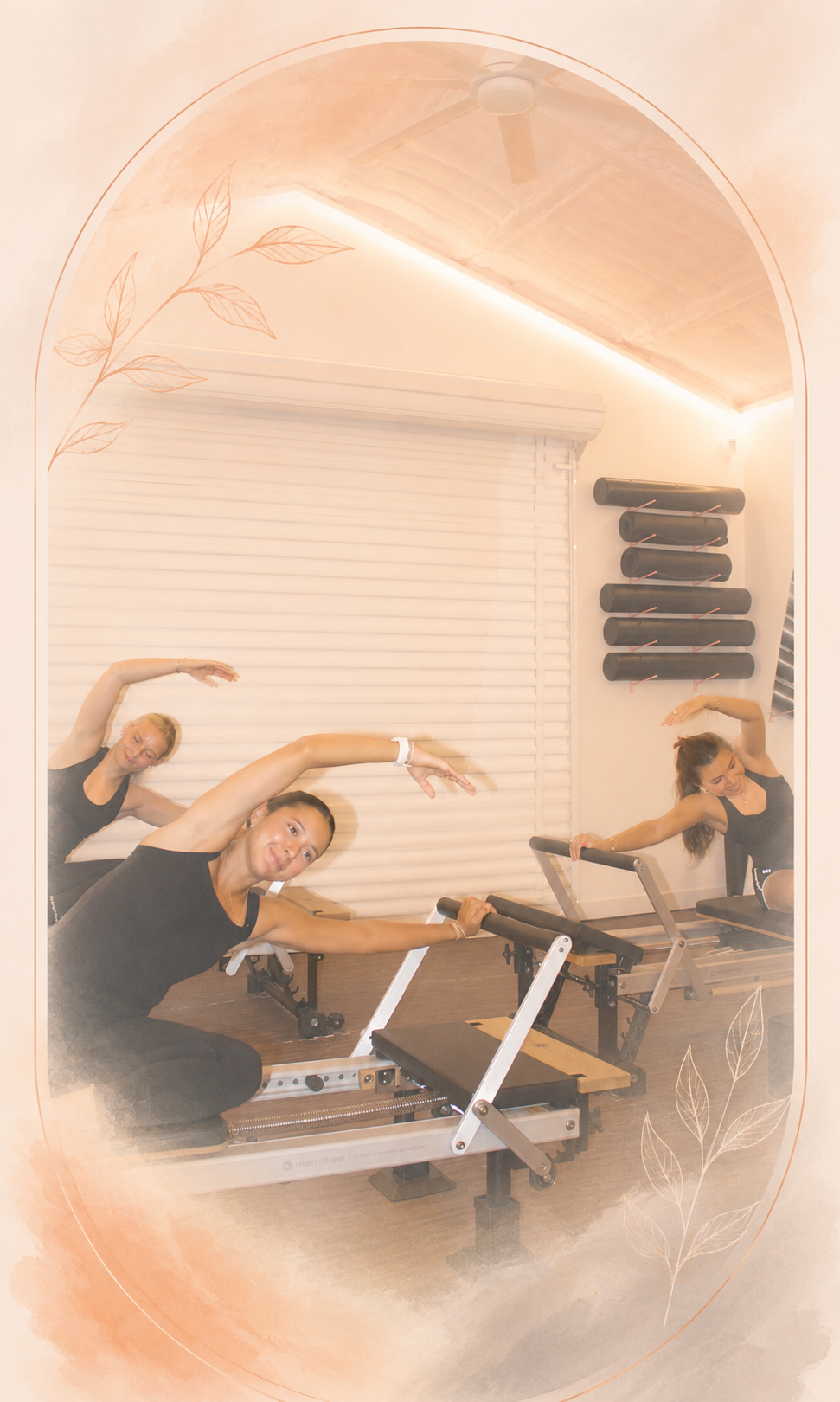 Three women stretching and exercising with Pilates reformers in a fitness studio, with exercise mats or rollers on the wall, and soft lighting.