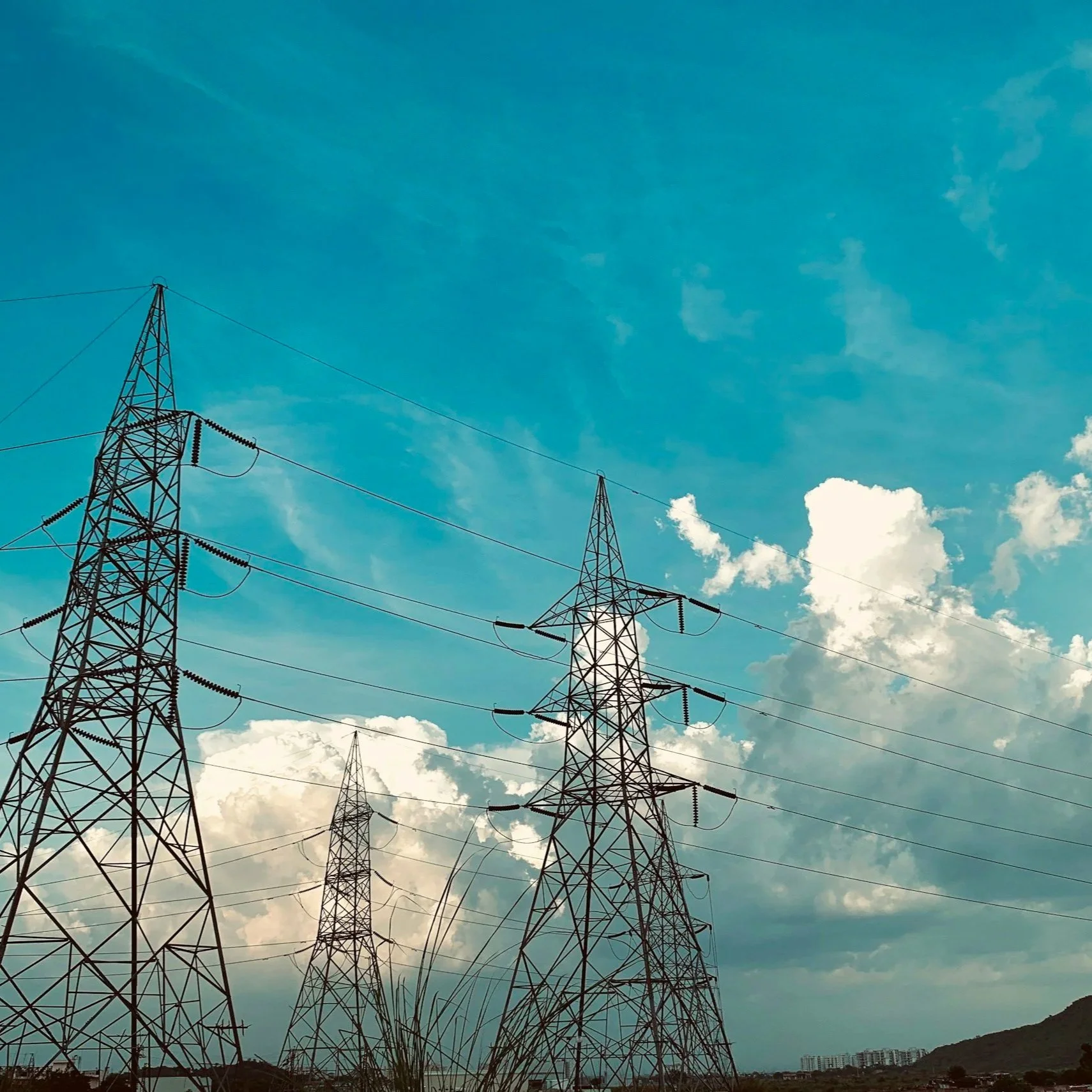 Electric transmission towers in a landscape with a blue sky and scattered clouds.