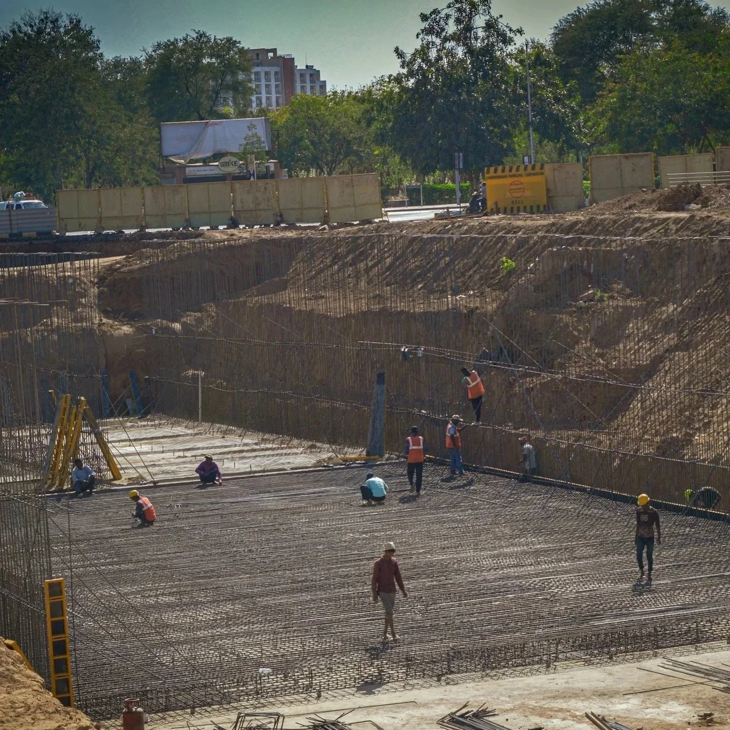 Construction workers are working on a building foundation at a construction site, with rebar and excavation in progress.