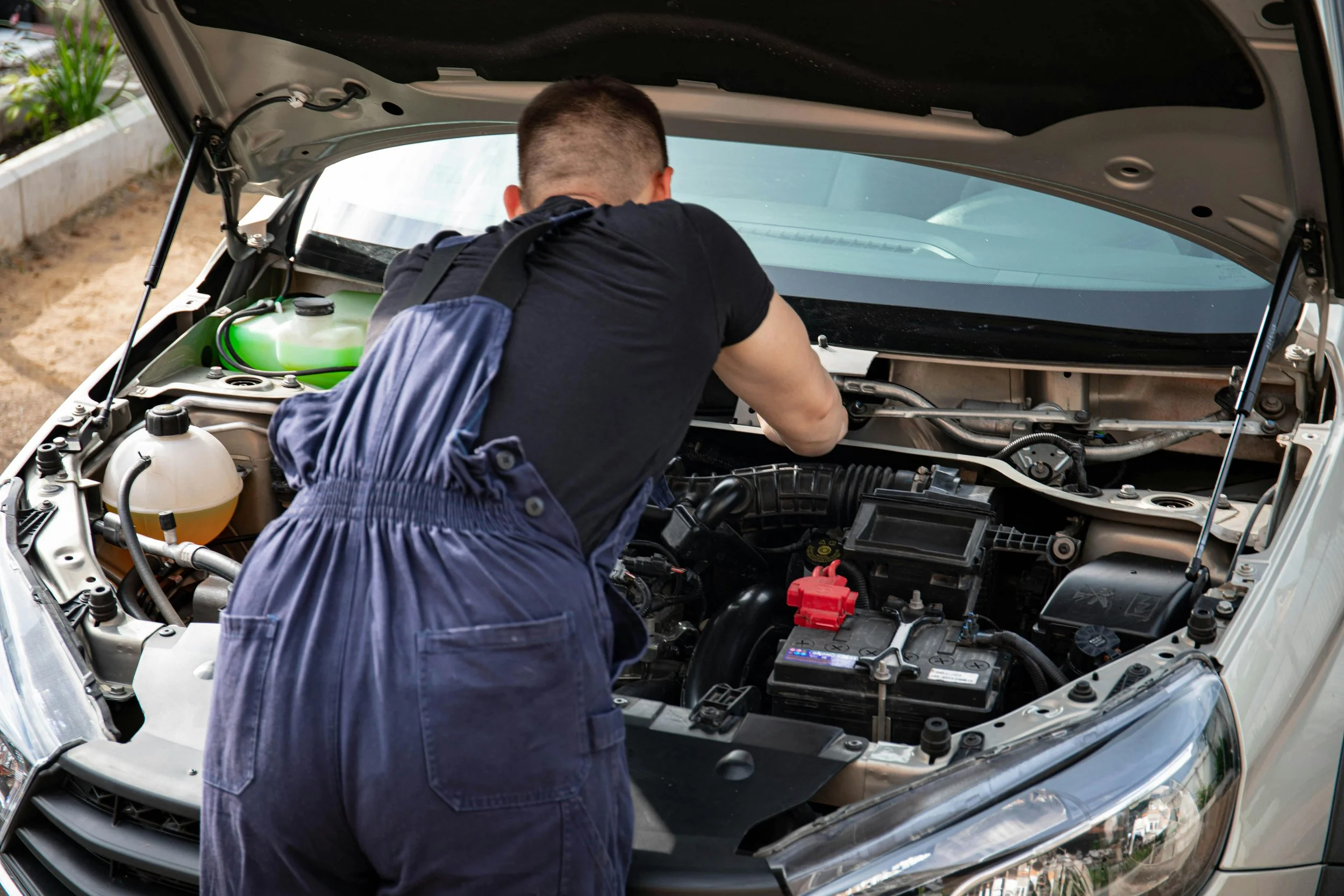 Man working on car engine with the hood open, inspecting or repairing it.