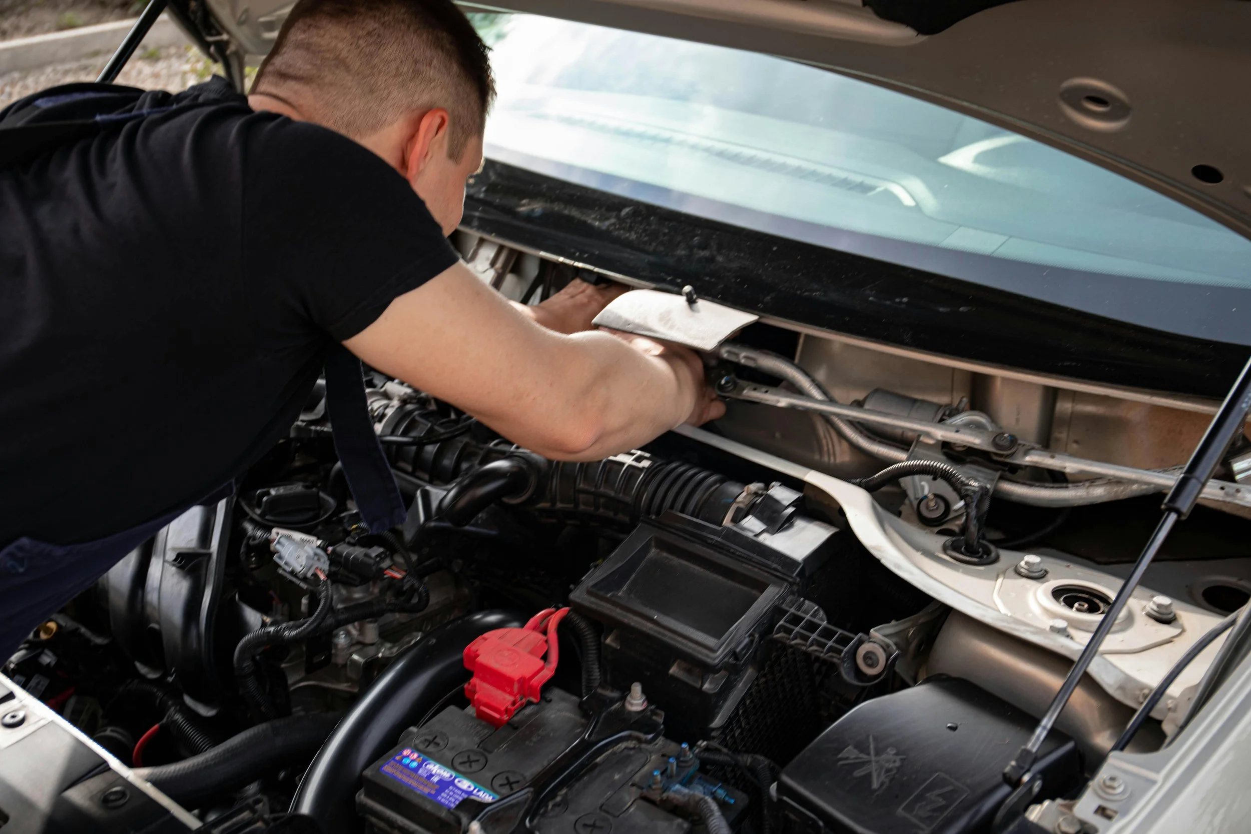 A man working under the hood of a car, repairing or inspecting the engine.