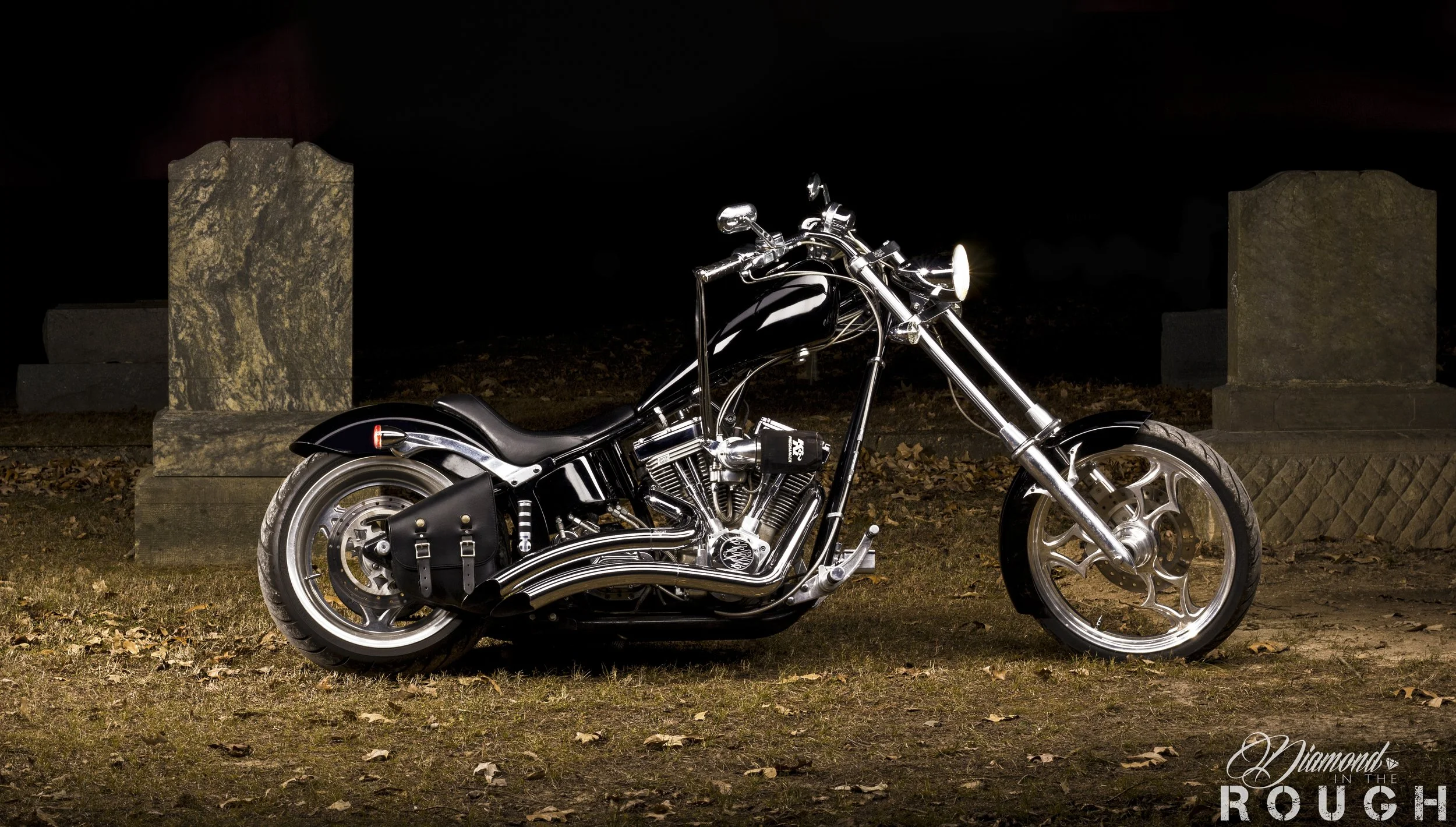 A shiny black and chrome motorcycle parked on grass next to stone columns at night.