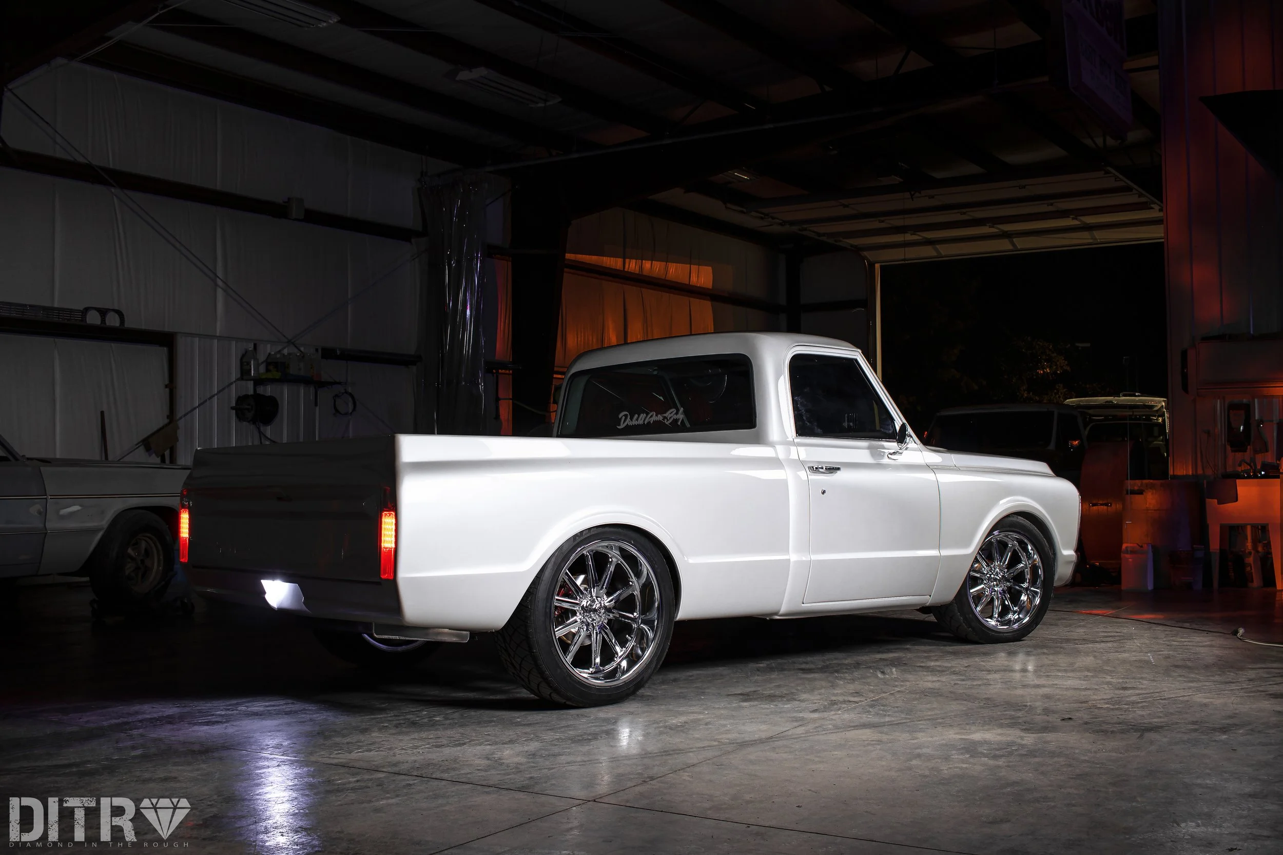 A white vintage pickup truck with custom wheels parked inside a dimly lit warehouse.