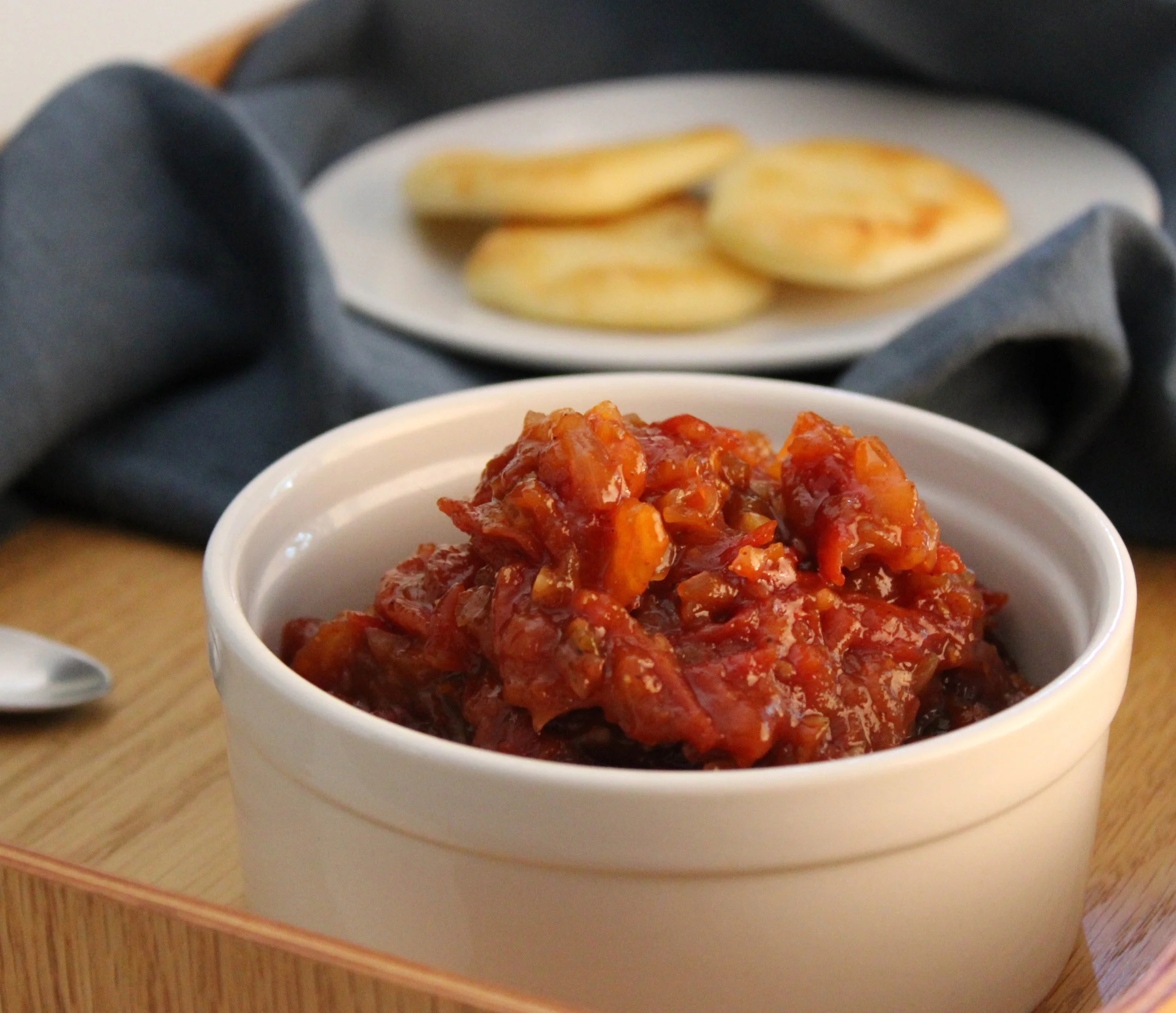 Close-up of a white bowl filled with spicy-looking simmered vegetables in a red sauce, placed on a wooden tray.