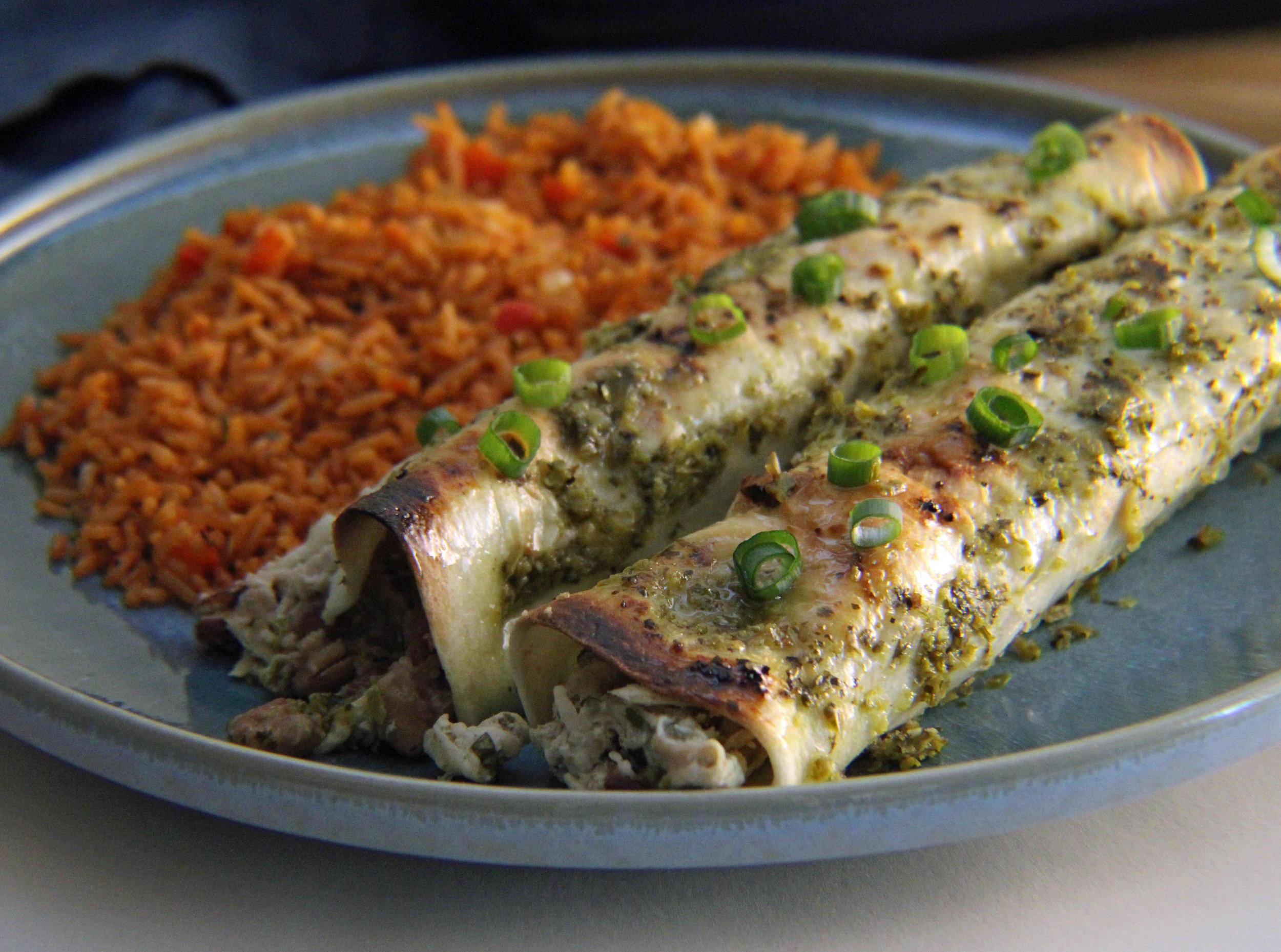 Close-up of grilled fish topped with chopped green onions and herbs, served with a side of seasoned rice on a grey plate.