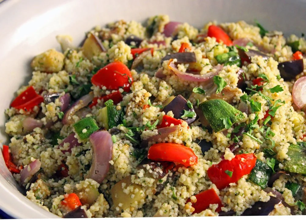 Vegetable couscous with roasted summer vegetables, fresh herbs and basil dressing served in a large white bowl.