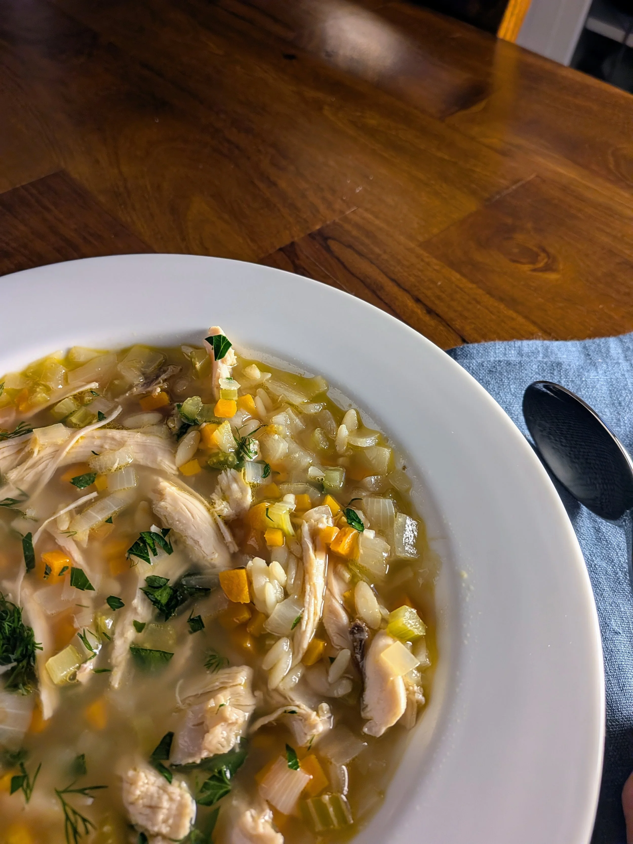 A bowl of chicken noodle soup with chopped vegetables and fresh herbs on a wooden table.