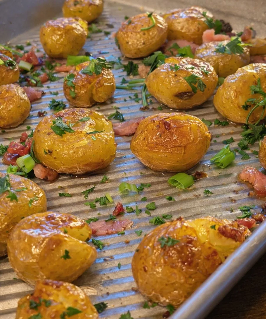 Crispy roasted baby potatoes with bacon, spring onions and fresh parsley on a baking tray.