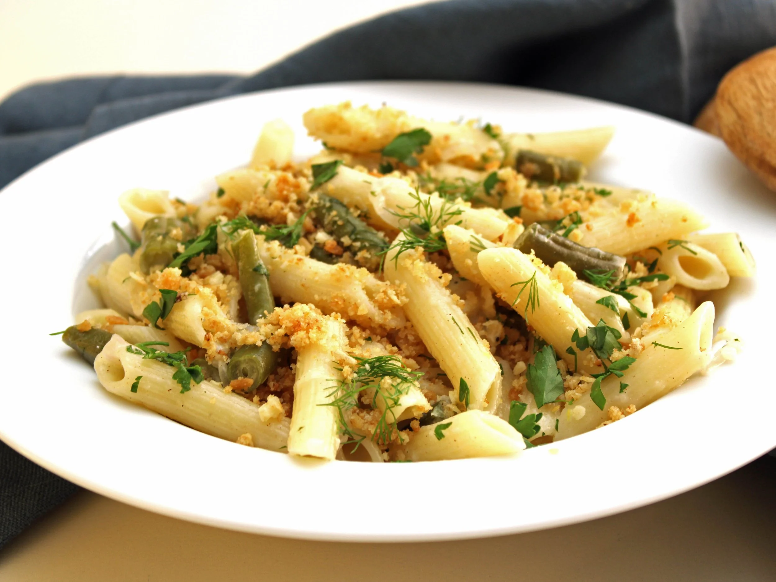 A plate of creamy pasta with green beans, herbs, and breadcrumbs.