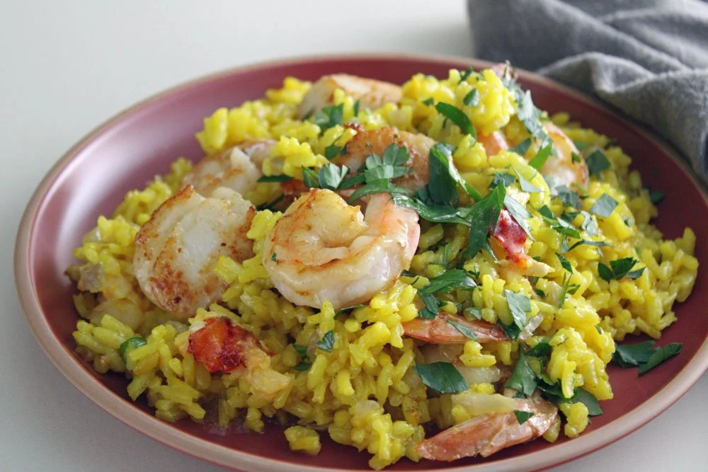 Creamy saffron seafood risotto with lobster, scallops and prawns served on a terracotta plate with fresh parsley and Parmesan for an elegant seafood dinner.