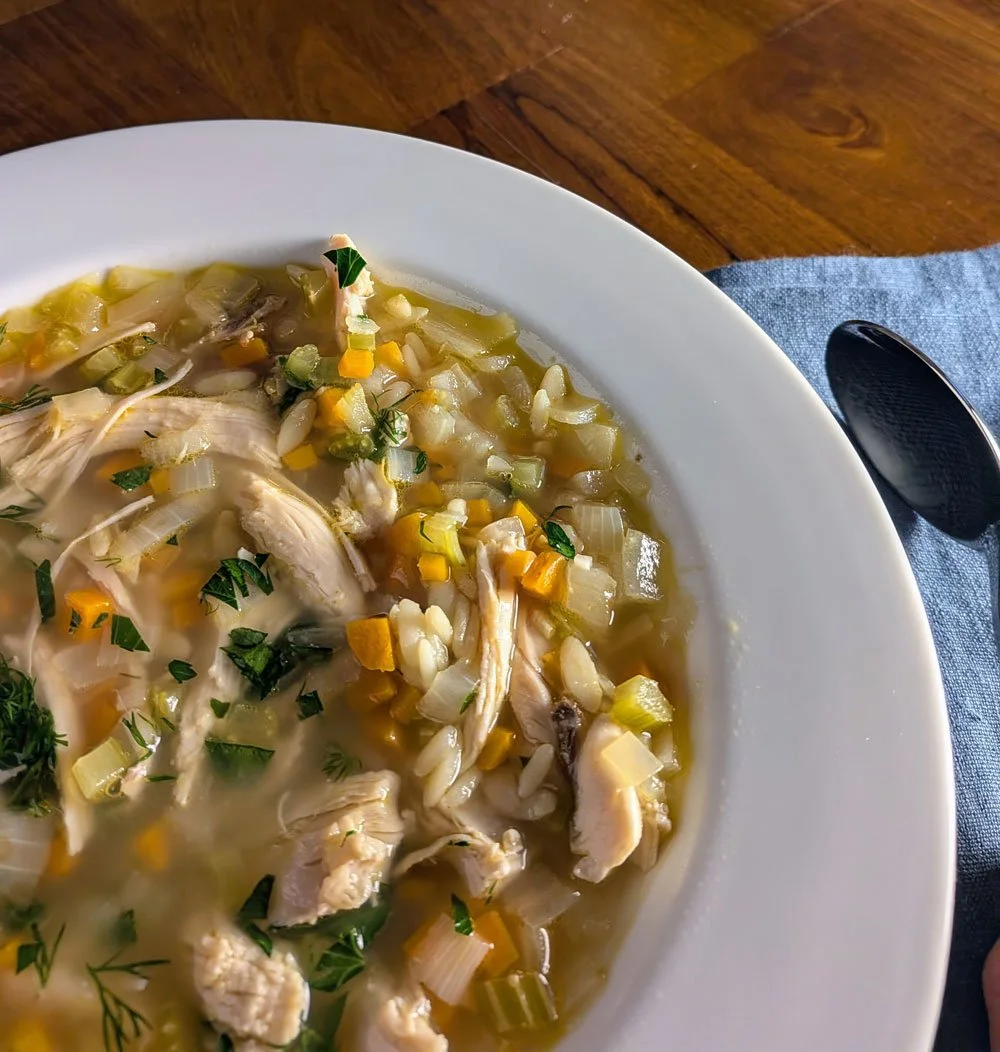 Chicken and rice soup with shredded chicken, celery, onion, carrots and fresh herbs in a white bowl.