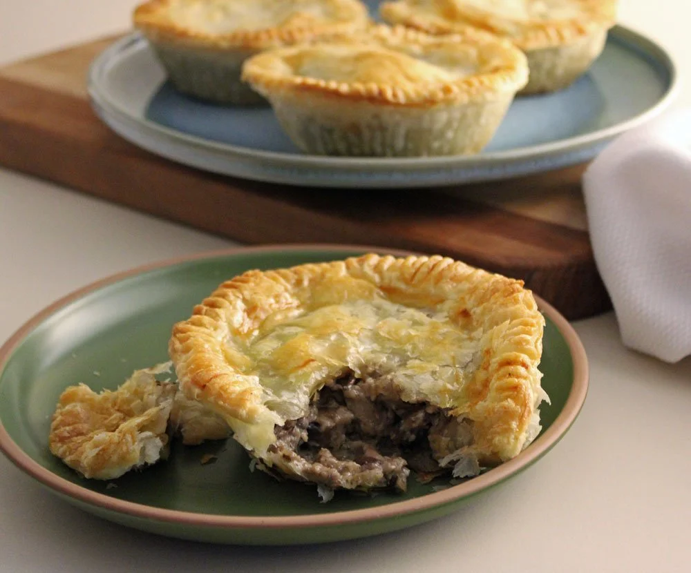 Creamy mushroom puff pastry pies with a rich baby bella and shiitake mushroom filling baked in crisp golden pastry, served on a green plate with one pie cut open to reveal the creamy centre.