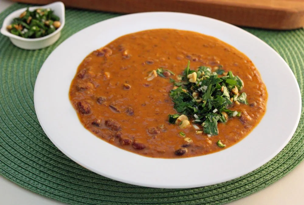 Smoky red bean soup with green sambal made with kidney beans, smoked paprika, and peanuts, served in a white bowl with a fresh herb topping.