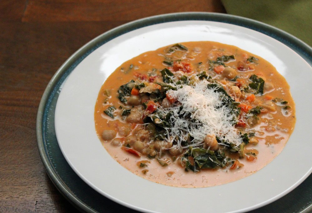 Creamy chickpea soup with kale, vegetables, and Parmesan, served in a shallow bowl with a rich, velvety broth and tender chickpeas.