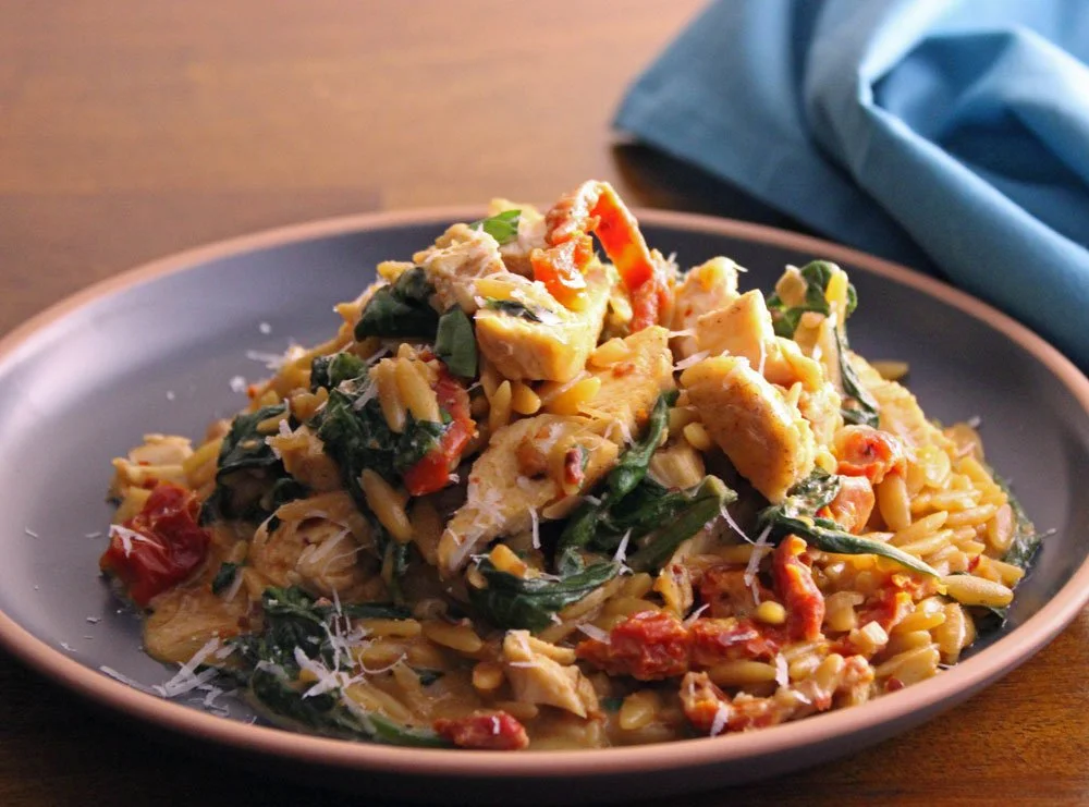 Ask Katie recipe for creamy Tuscan chicken orzo served in a grey bowl with chicken, spinach, sun-dried tomatoes, Parmesan and creamy orzo pasta.