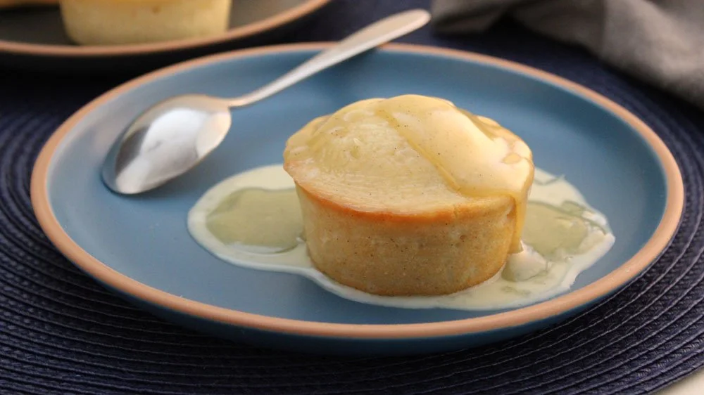 South African malva puddings with cream sauce served warm on a blue plate, with soft apricot sponge soaked in a rich vanilla cream sauce.