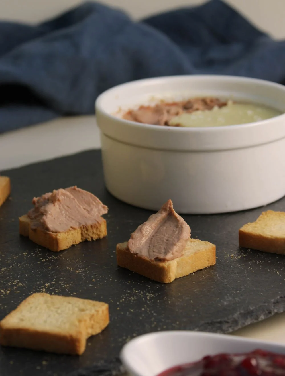 Creamy chicken liver parfait served with crisp crostini and fruit preserve on a slate serving board.