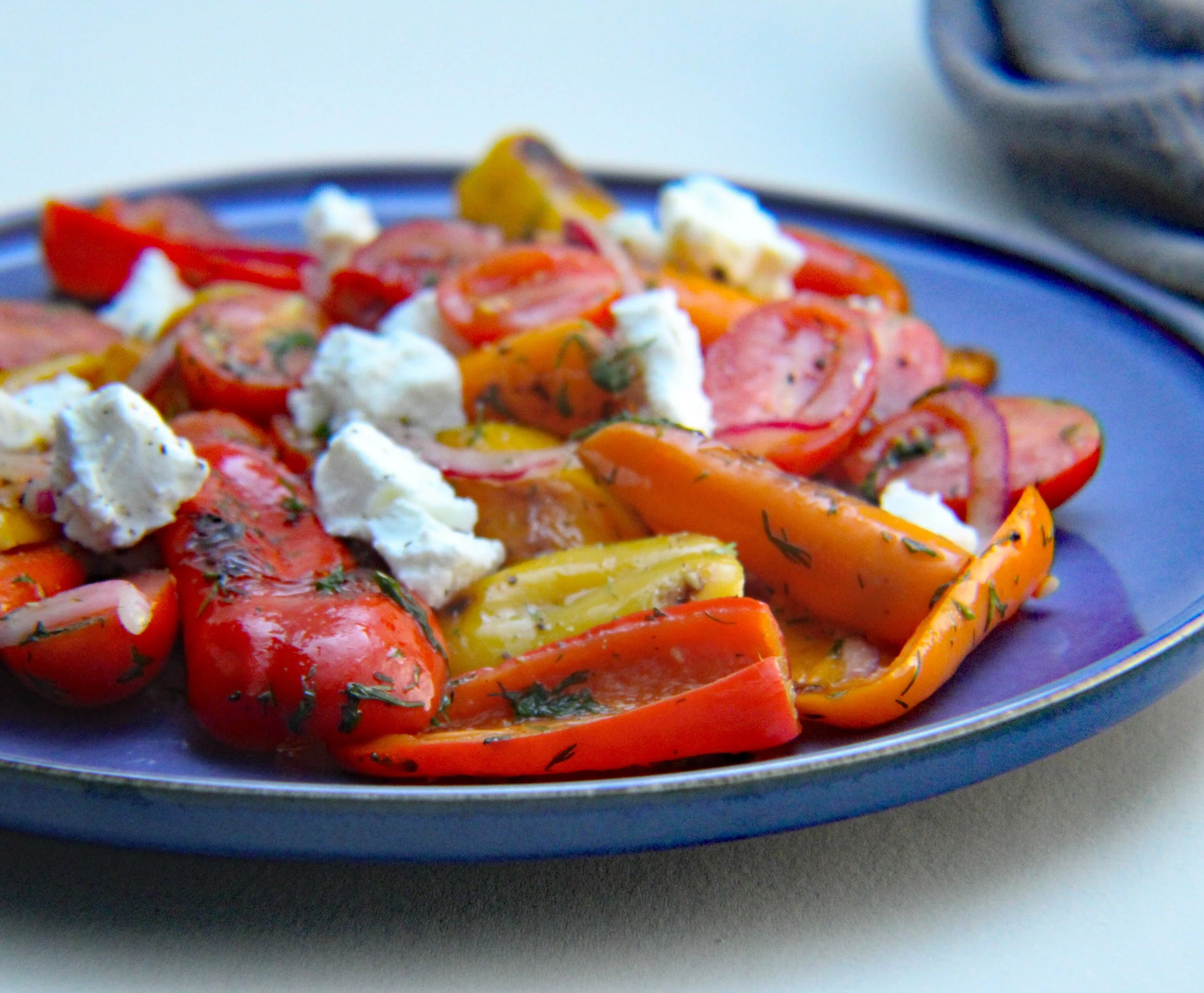 Close-up of roasted red and yellow bell peppers on a dark plate with dollops of creamy white cheese or mayonnaise.