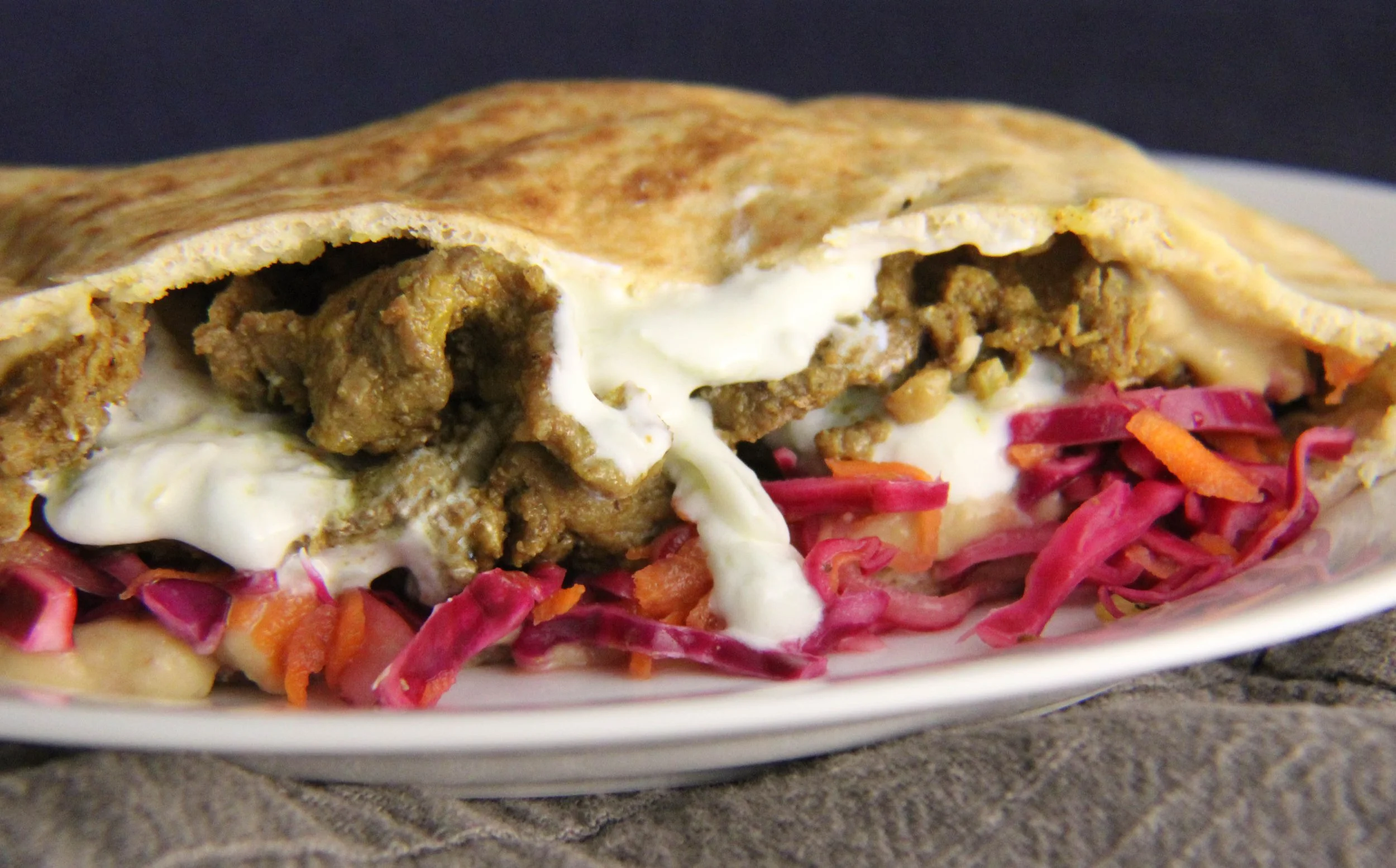 Close-up of a wrap sandwich stuffed with ground meat, melted cheese, shredded carrots, and purple cabbage, served on a white plate.