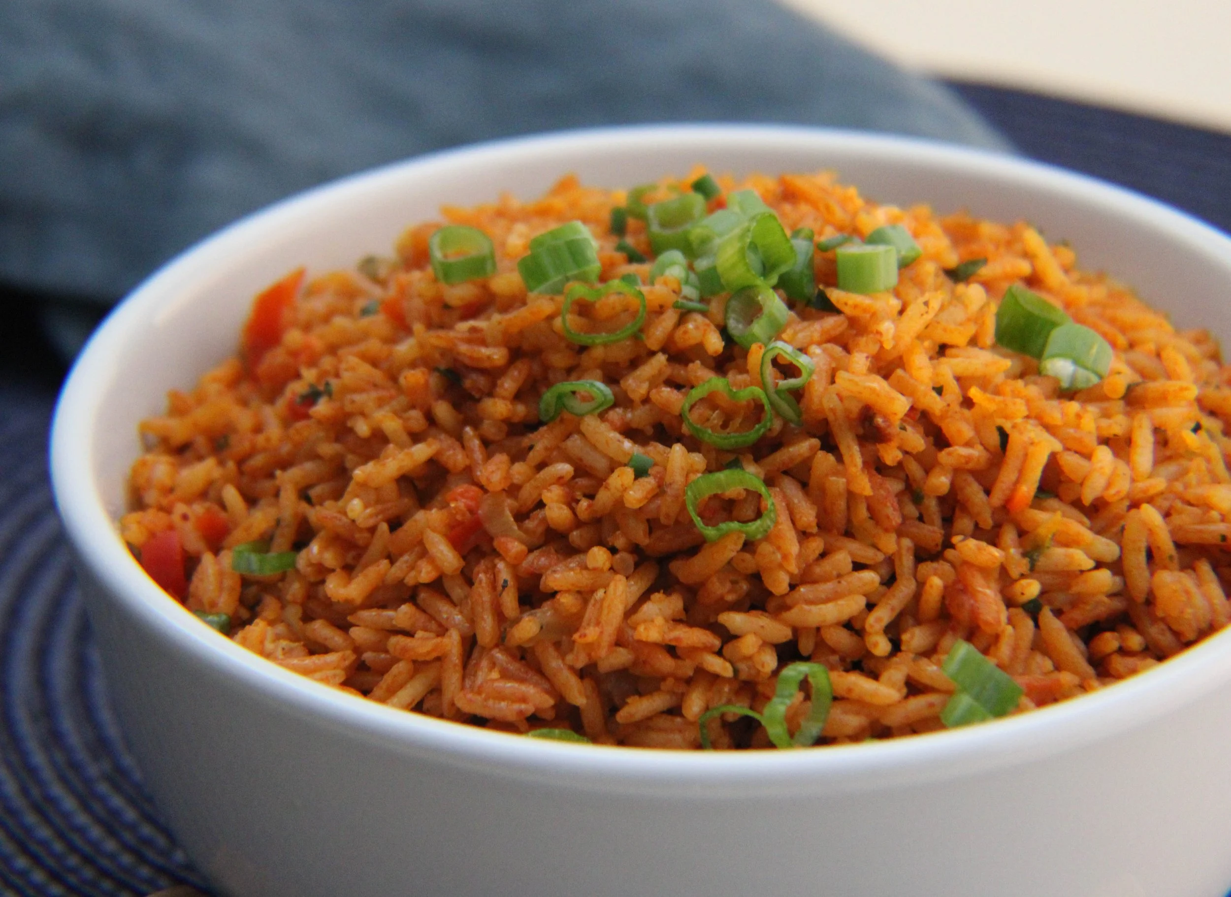 Close-up of a bowl of fried rice garnished with chopped green onions, placed on a dark textured surface.