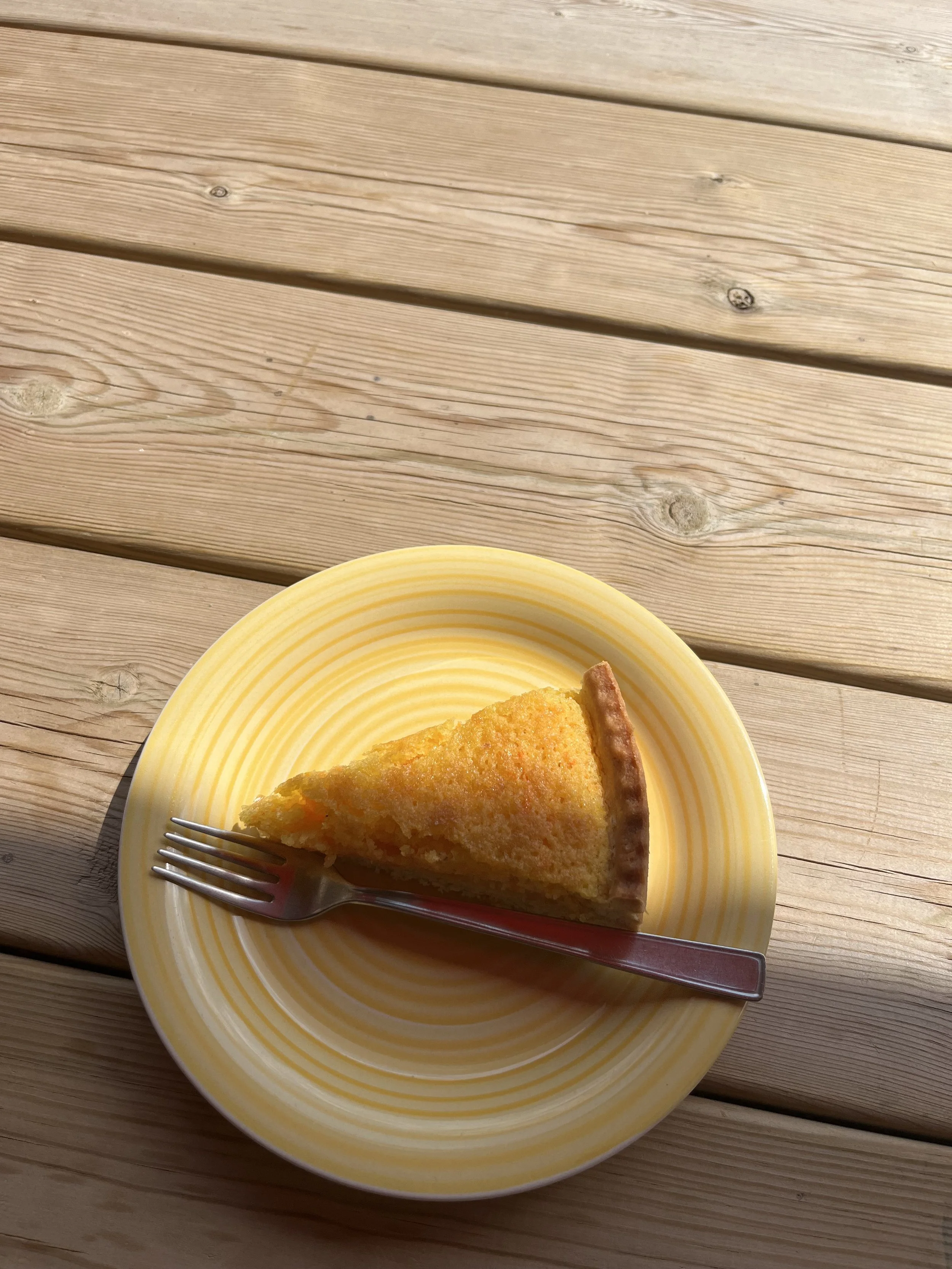 Slice of yellow cornbread or cake on a yellow and white striped plate with a fork resting on the plate, placed on a wooden table.