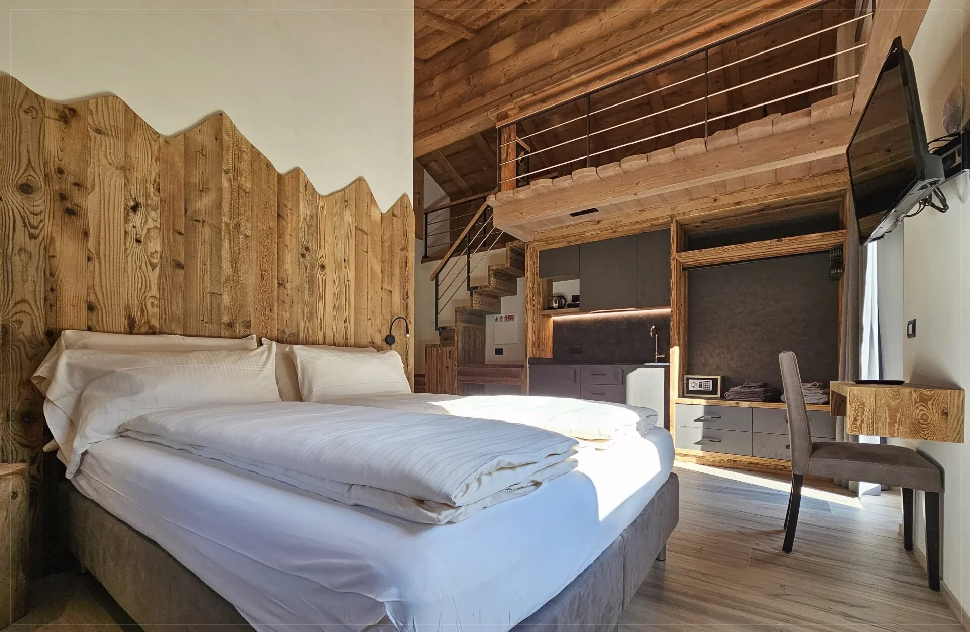 Hotel room with bed, wooden wall panels, kitchenette, and balcony with railing.