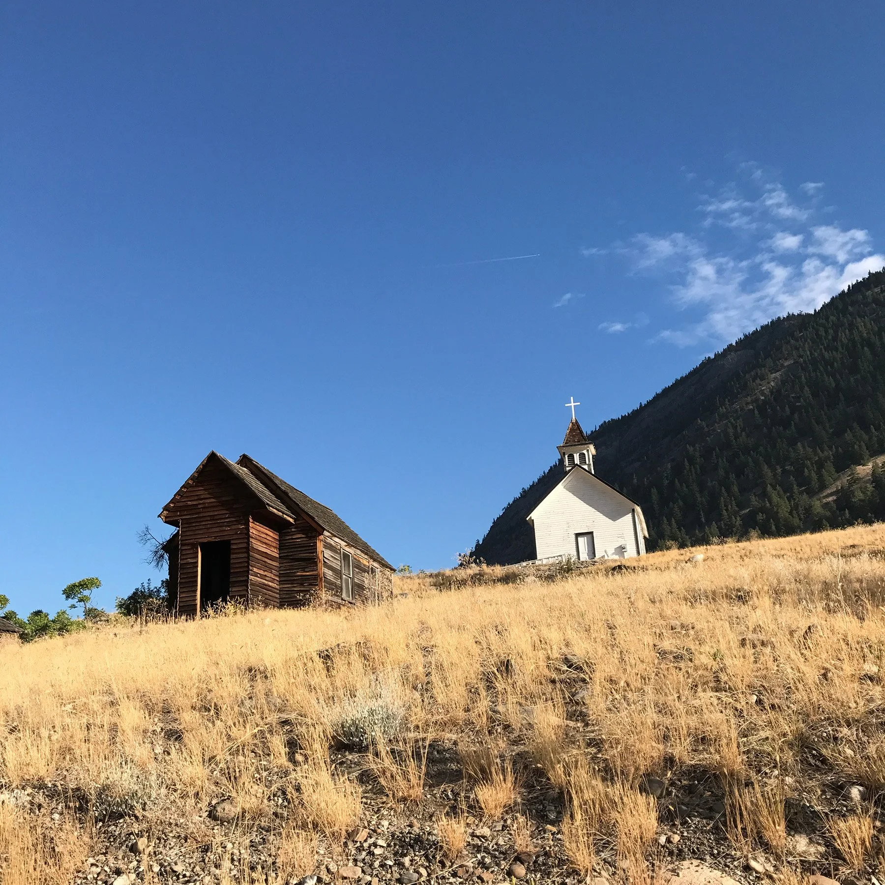 Old church and log cabin on a sunny grassy hill