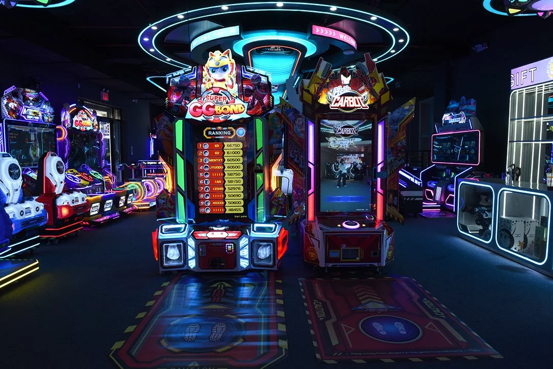 Indoor arcade with colorful neon lights and electronic games, including a basketball shootout and coin pusher machines.