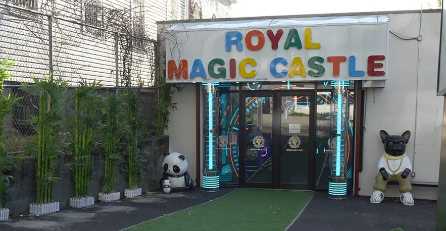 Entrance to Royal Magic Castle with colorful sign, panda and dog statues, and neon lights.