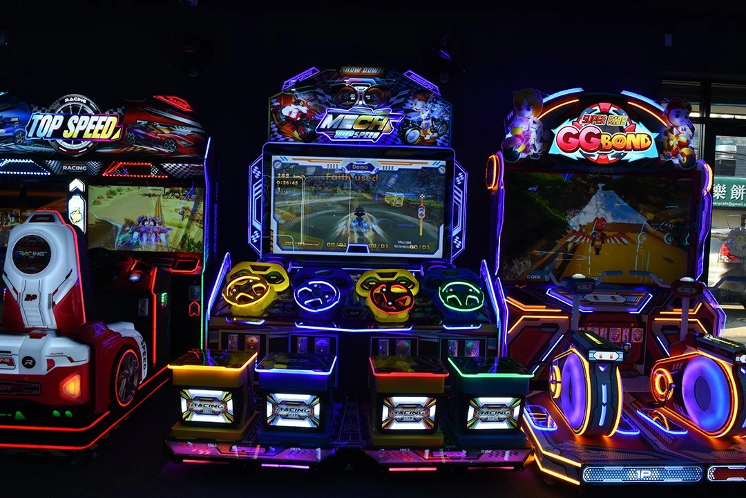 A row of colorful arcade racing game machines with screens displaying racing scenes and glowing control panels.