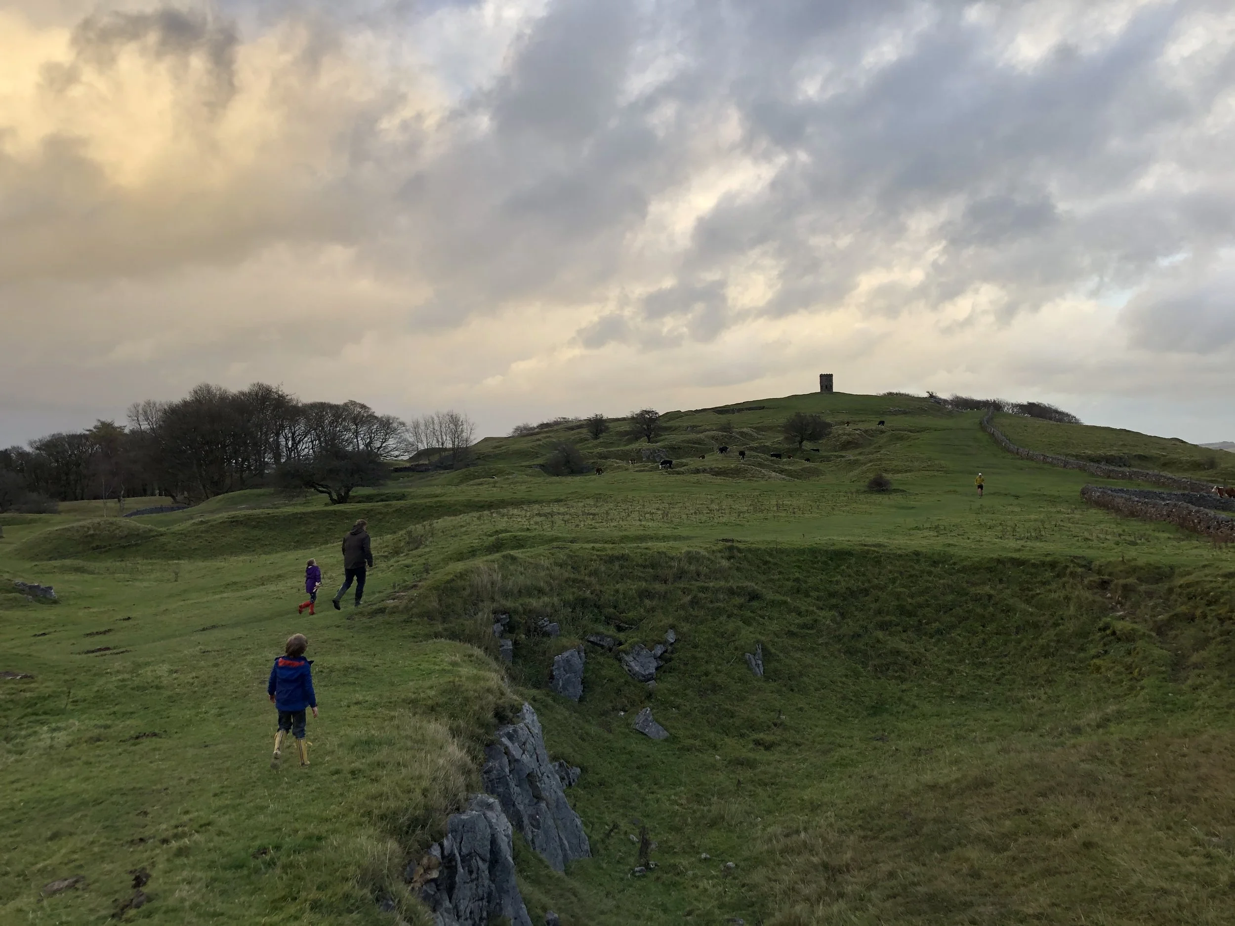 A family walking up the grassy hillside of Grin Low towards Solomon's Temple in the distance, a popular walking route near our Buxton holiday home.