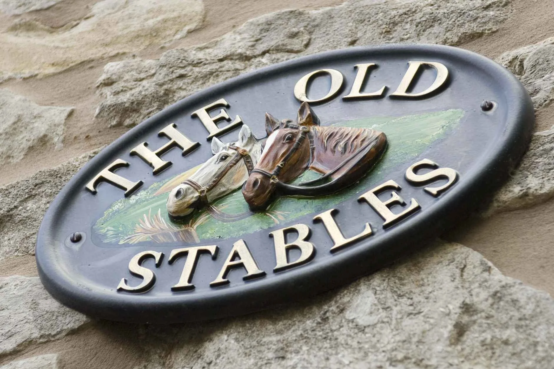 House sign for 'The Old Stables' in Buxton, featuring a decorative motif of two horses, reflecting the building's heritage as 18th-century Duke of Devonshire stables.