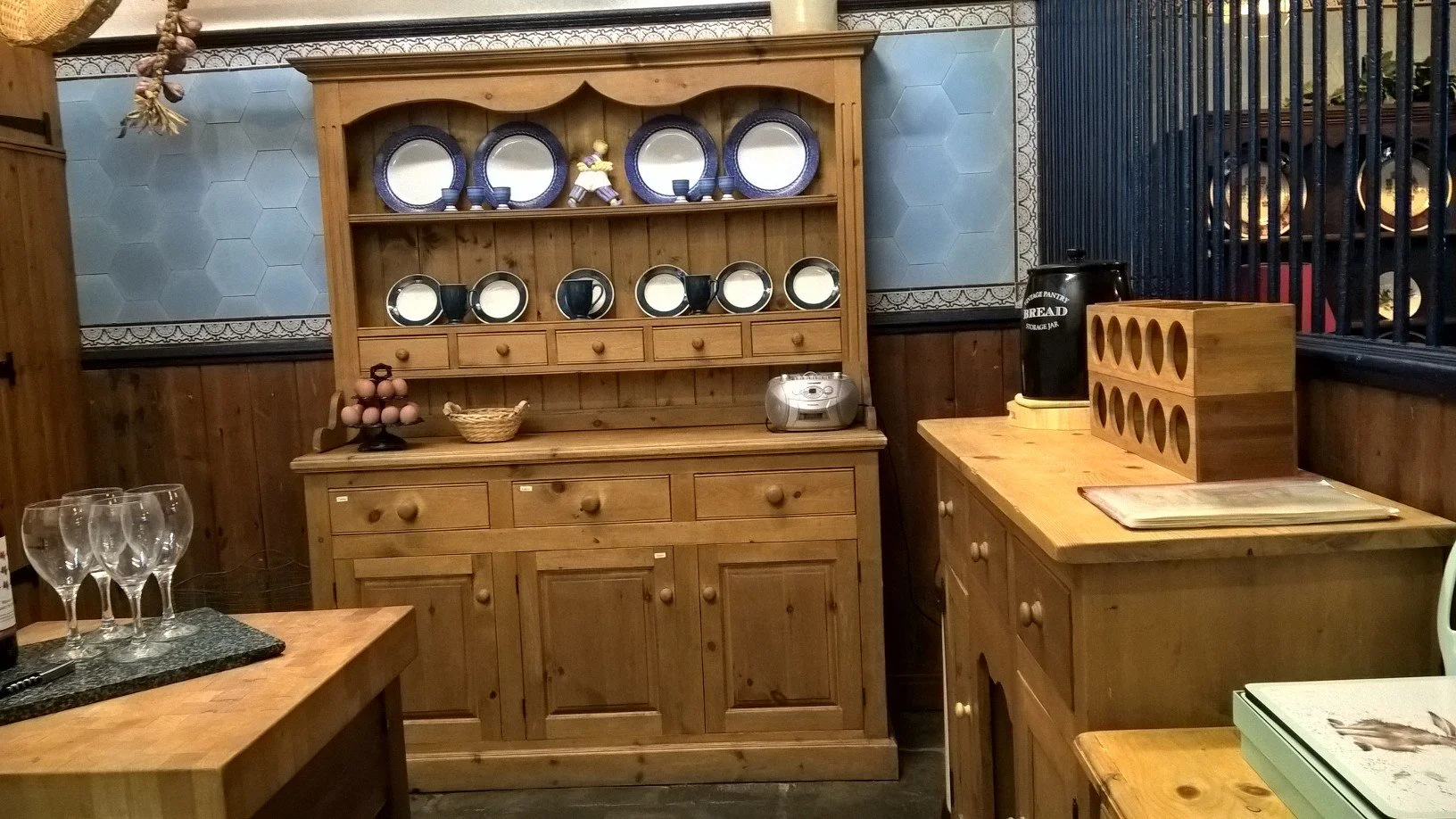 Wooden kitchen cabinetry and open shelving at The Old Stables Buxton, displaying matching plates and cups alongside a bread storage jar and tray on a clean countertop."