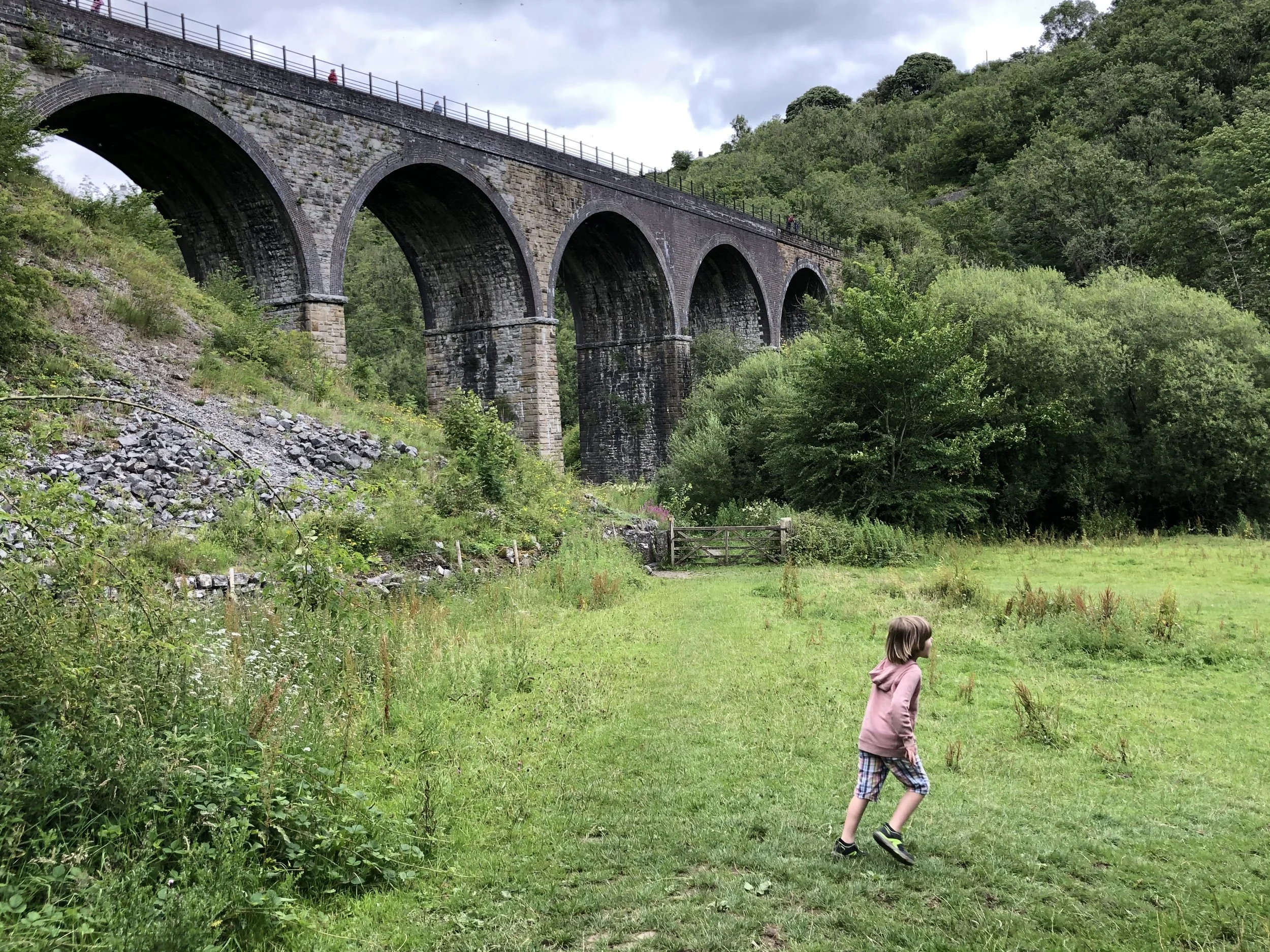 A boy running along the path at Monsal Head viewpoint overlooking the Headstone Viaduct, a popular day trip for families staying in Buxton.
