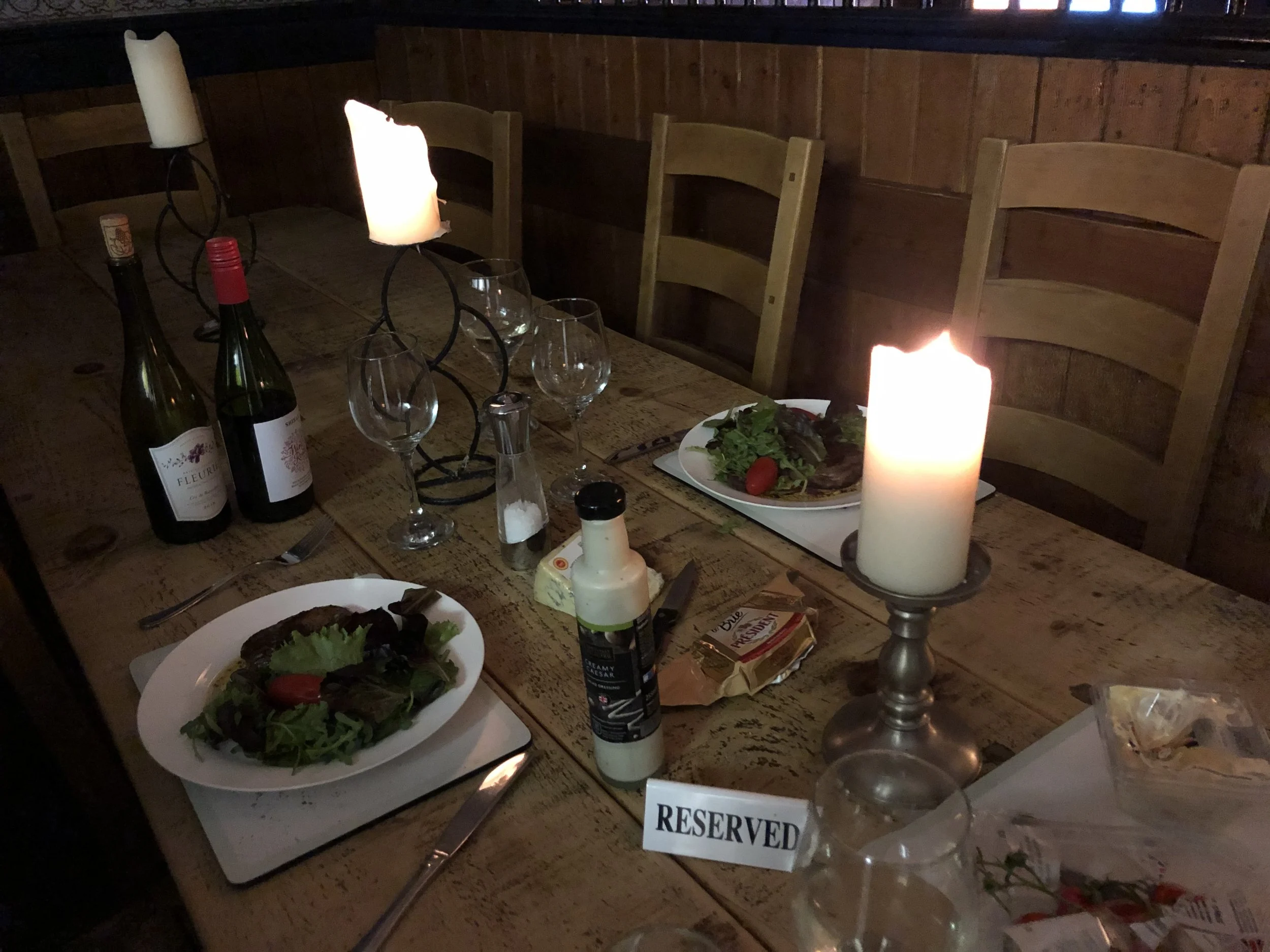 A close-up of a rustic wooden dining table at The Old Stables Buxton, elegantly set with salad plates, wine glasses, candles, and a playful 'Reserved' sign