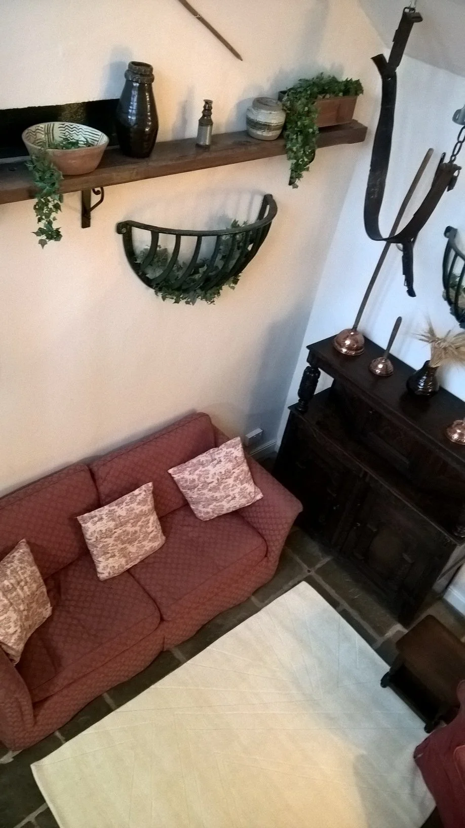 A cosy corner of the living room at The Old Stables Buxton, featuring a red patterned sofa with cream cushions, a dark wood cabinet, and unique equestrian-themed wall decor including vintage leather and metal stable tackle.
