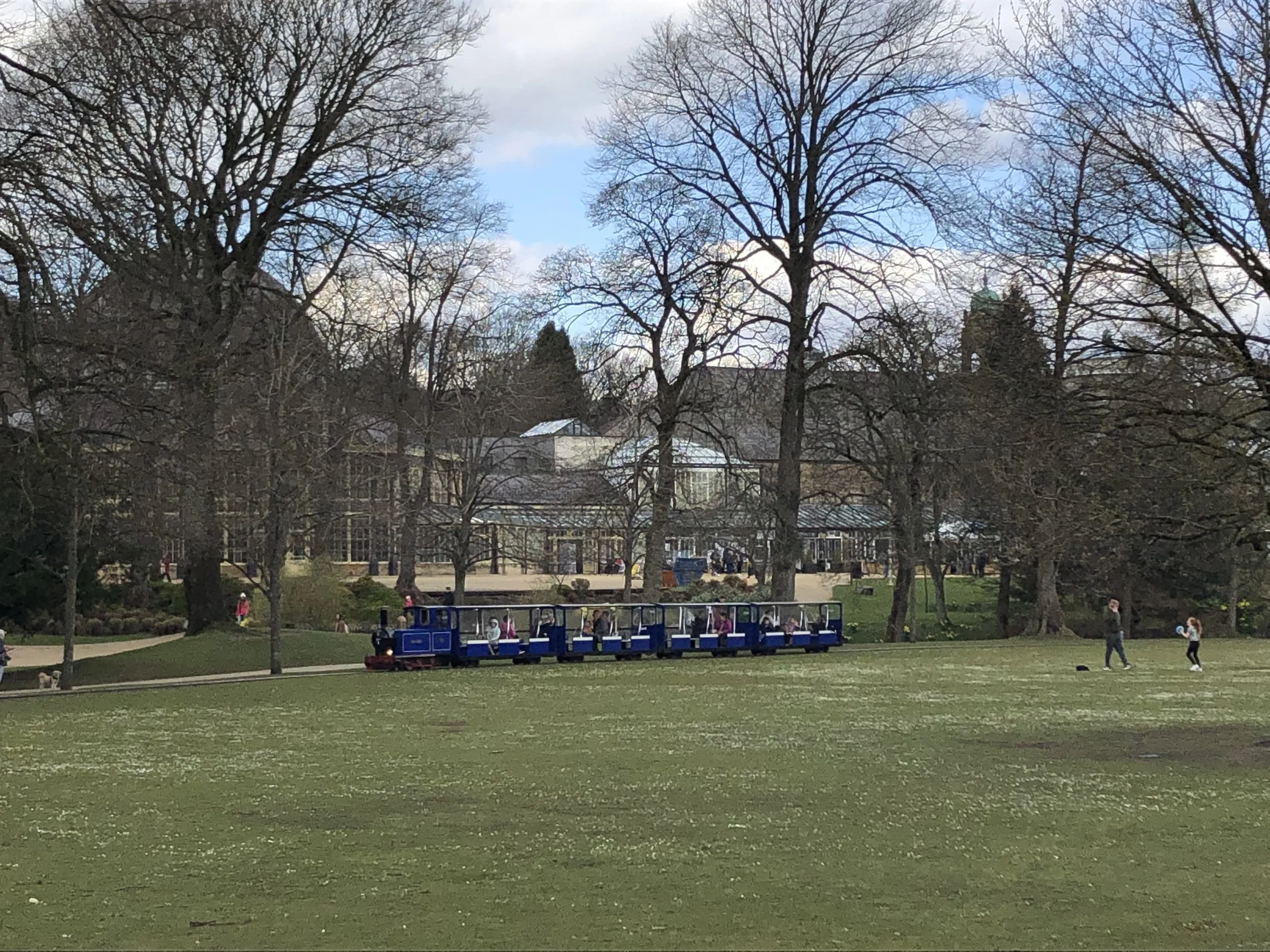 The iconic miniature train traveling through the Buxton Pavilion Gardens with the historic Pavilion building and Octagon in the background.