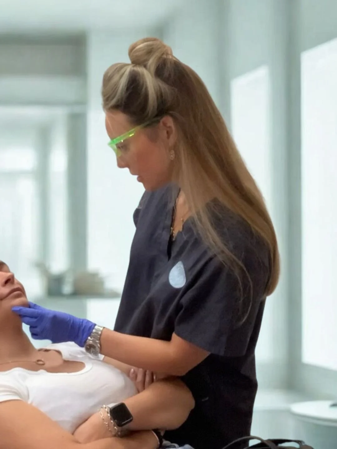 Dental professional wearing protective glasses and gloves examining a patient in a clinical setting.