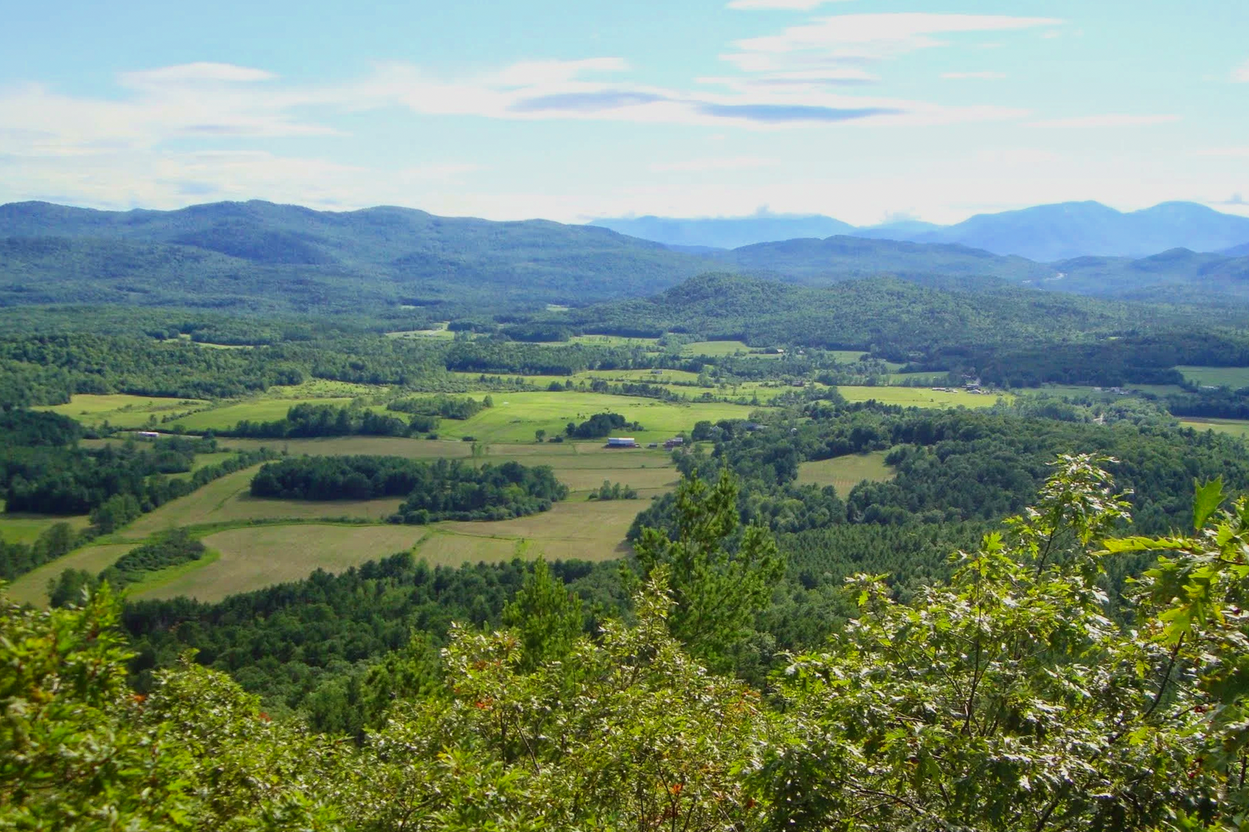 A sunny view of an Appalachia valley with blue mountains in the background.