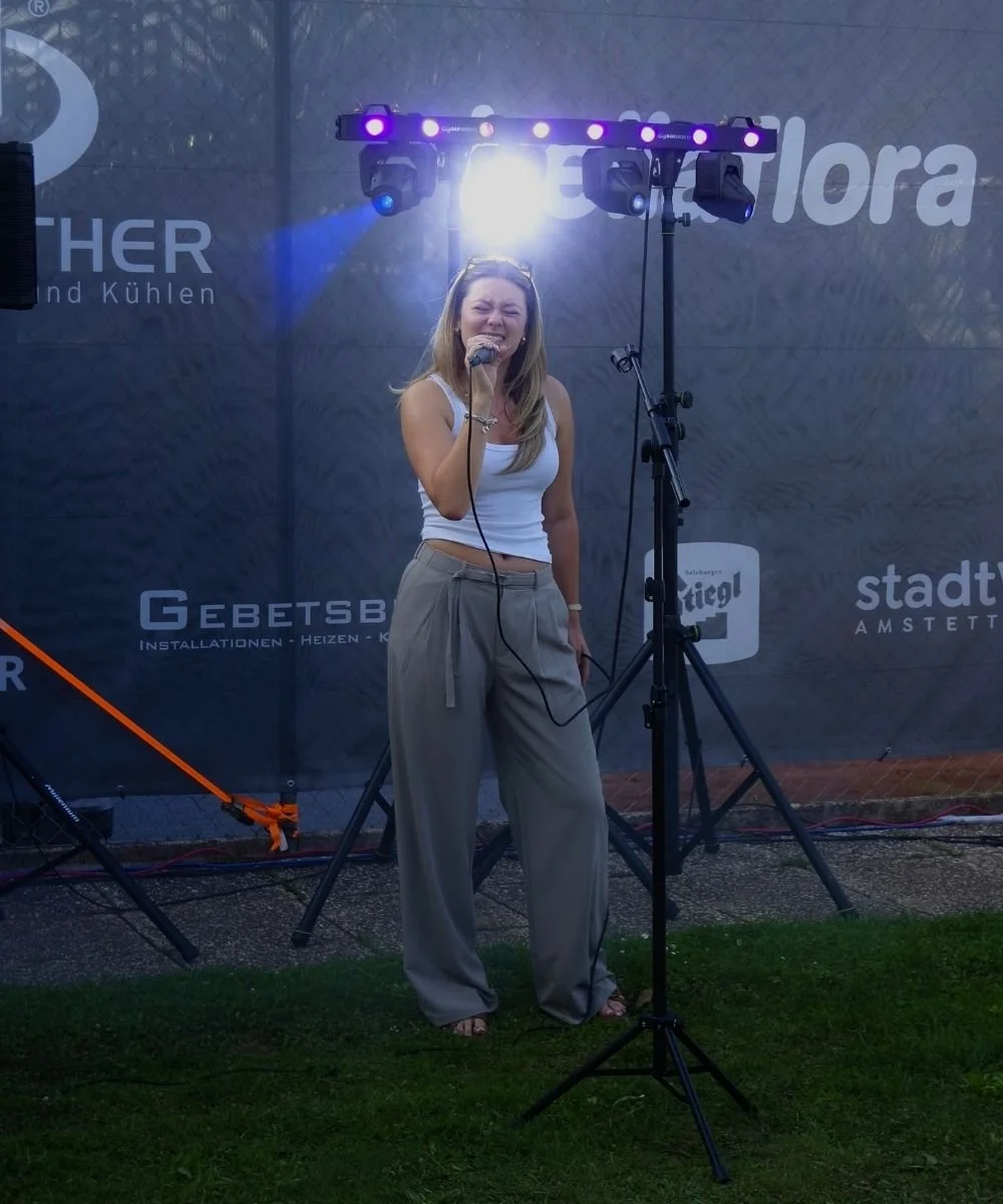 Tasmina Valentina,  eine junge Künstlerin aus dem Mostviertel, singt in einem Mikrofon auf einer Bühne beim After-Tennis-Clubbing im Rahmen der LADIES OPEN Amstetten.